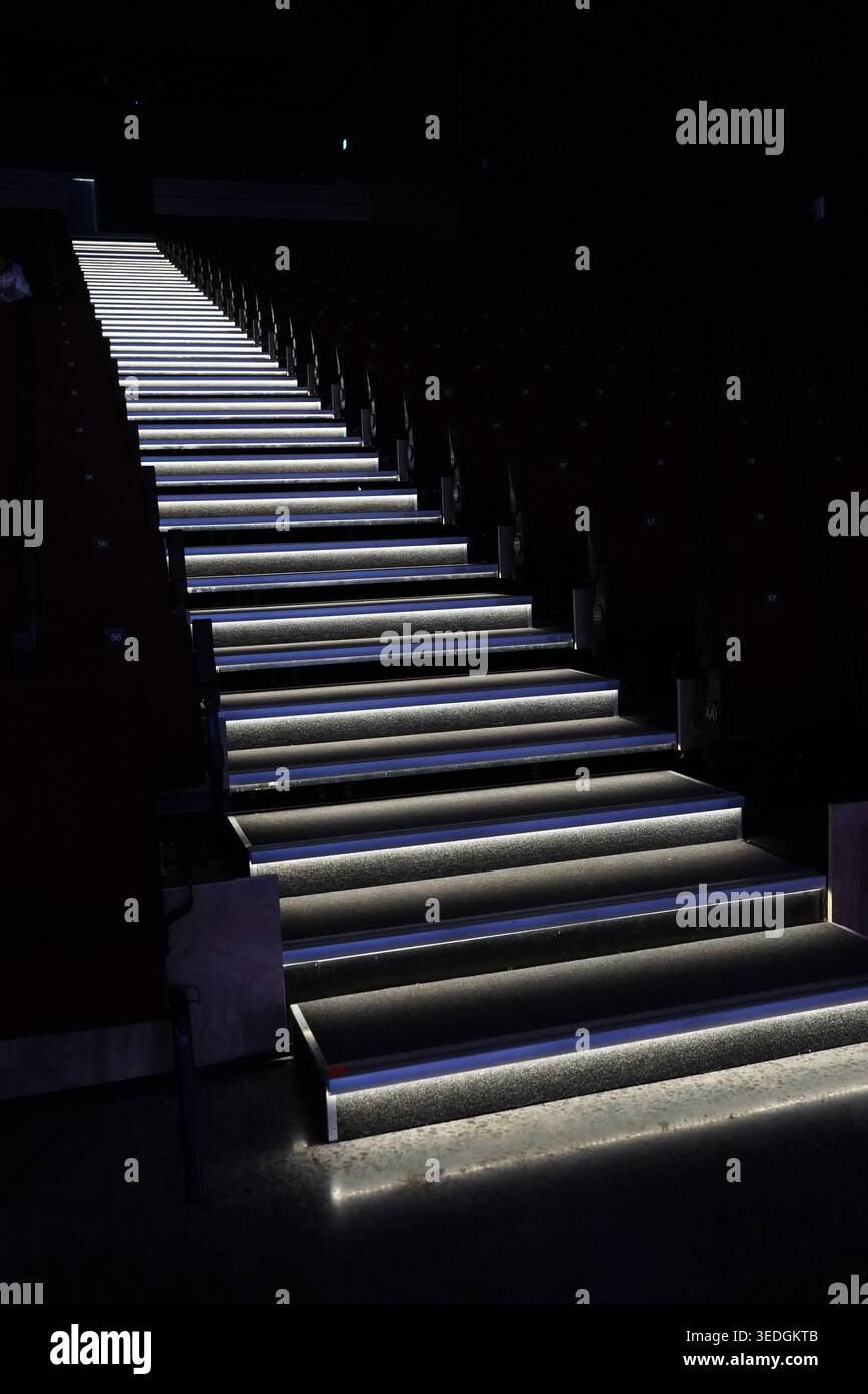 Interni cinematografici scuri con scala con illuminazione di sicurezza a strisce LED, sedili vuoti rivestiti di colore rosso e design moderno del teatro. Foto Stock