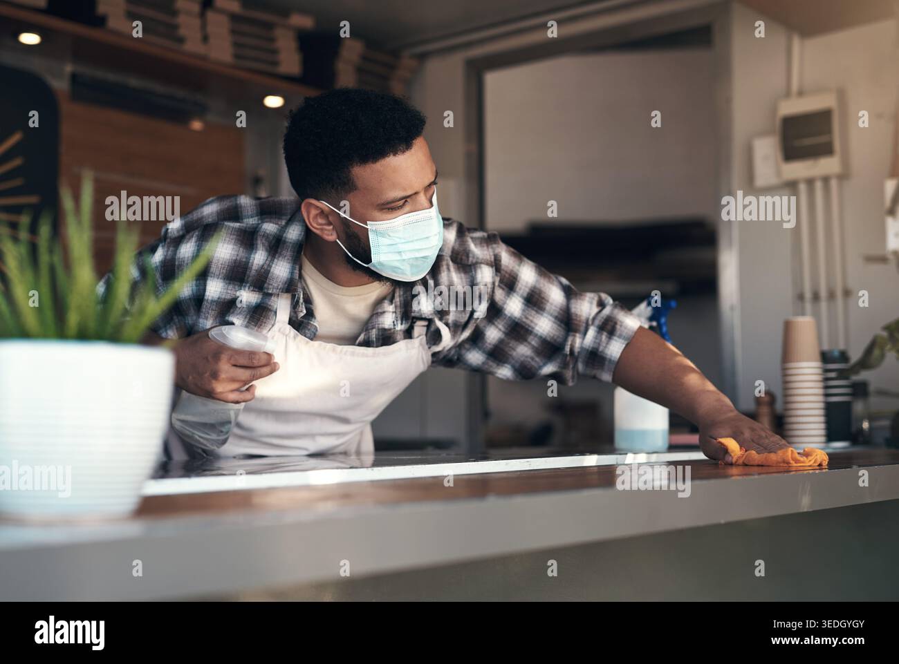 Igienizzare, ristorante e uomo con panno, pulizia contatore e disinfettante per antibatterico. Imprenditore, persona e dipendente con maschera facciale per Foto Stock