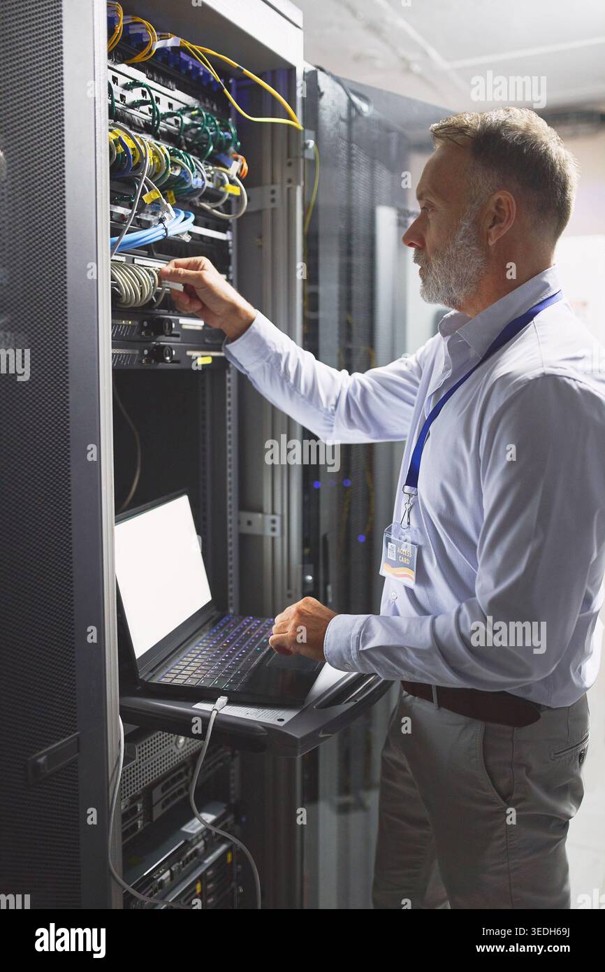 Sala server, ingegnere e connessione con notebook per sicurezza informatica, manutenzione o archiviazione digitale. Persona matura, rete di intelligenza artificiale o apprendimento automatico per Foto Stock