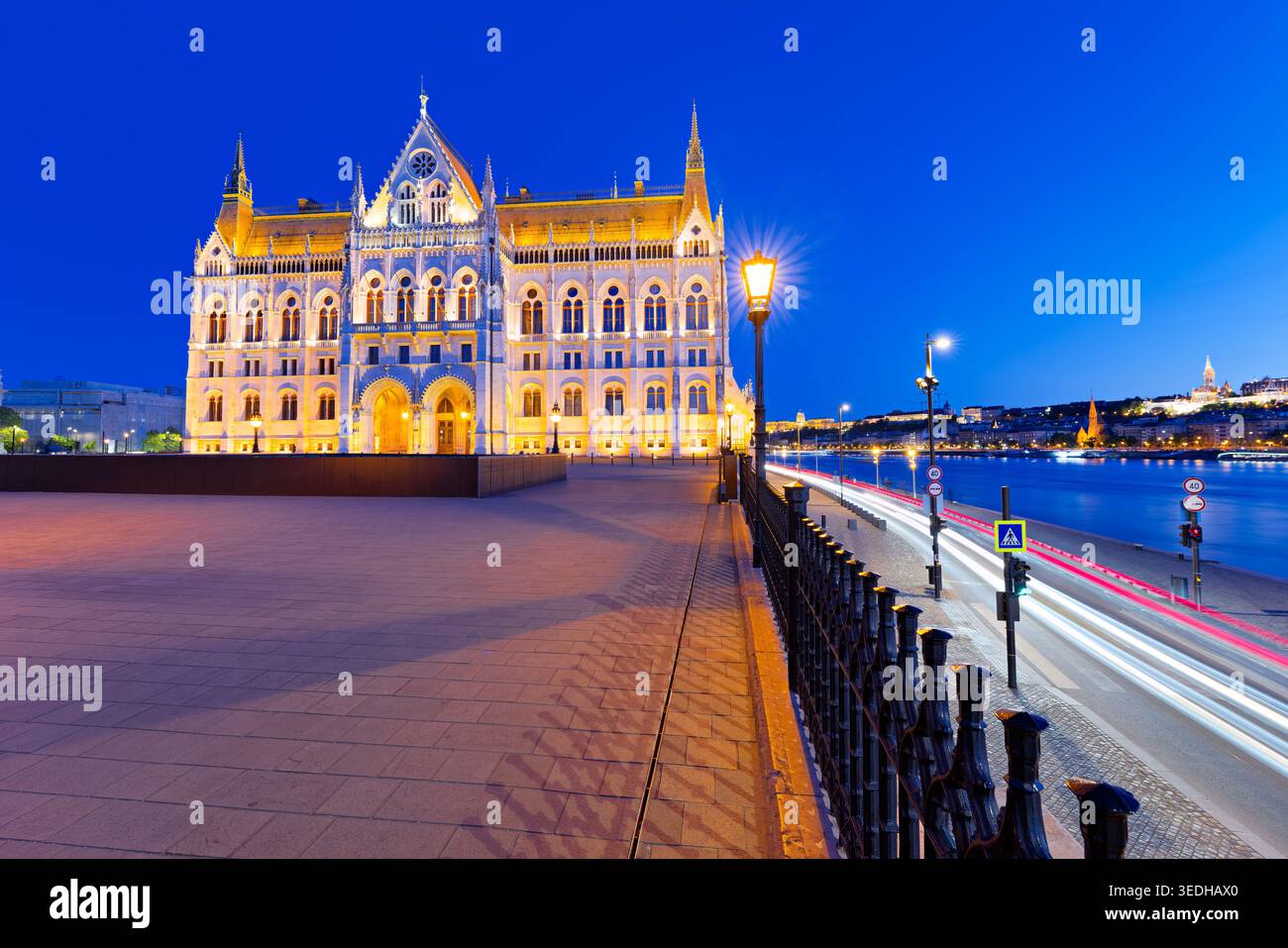 L'edificio del Parlamento di Budapest si illumina al tramonto. La gente cammina lungo il fiume mentre le auto si muovono sullo sfondo mentre il giorno diventa notte. Foto Stock