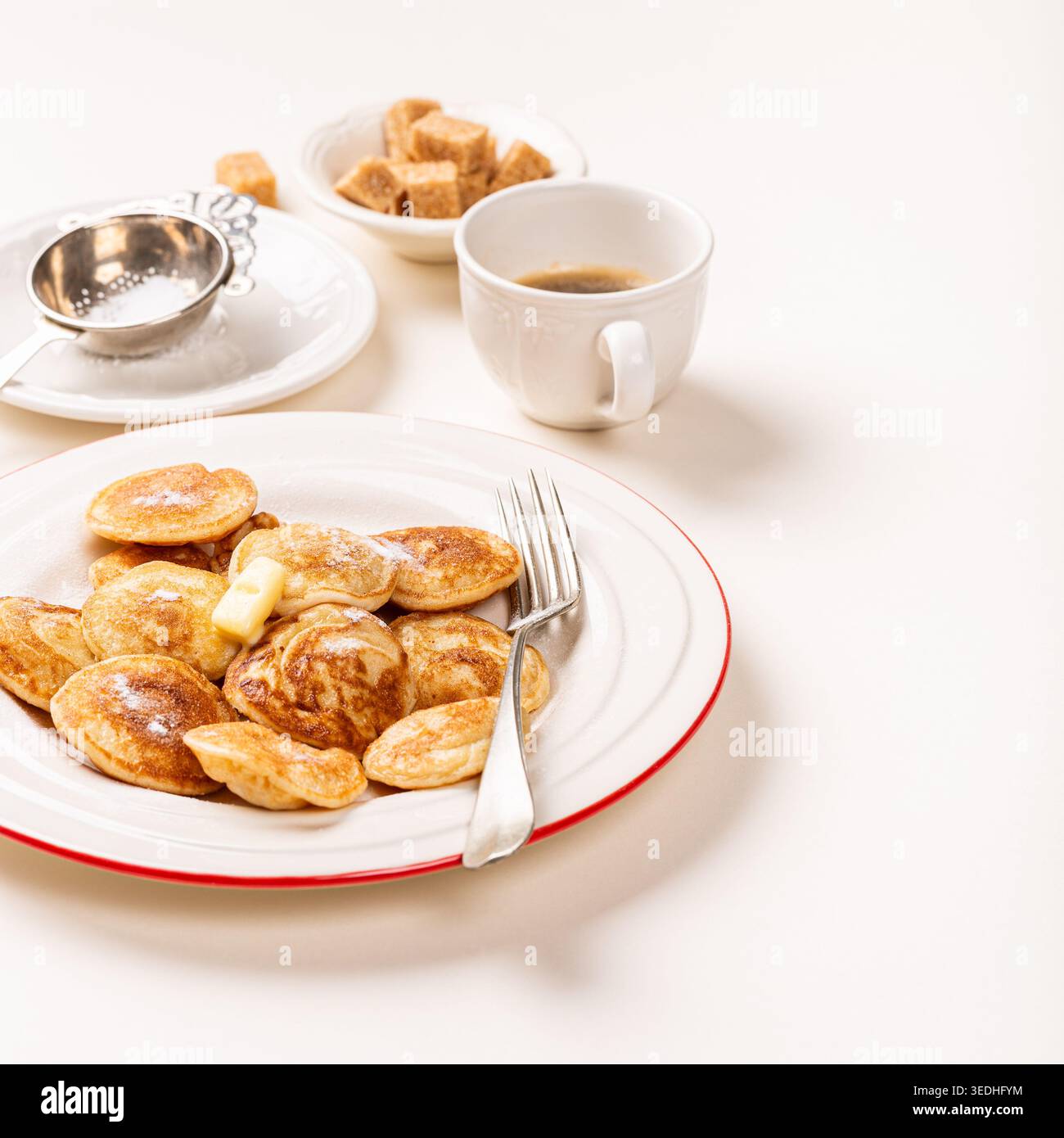 Piccoli pancake olandesi poffertjes serviti con burro, cubetti di zucchero e caffè su sfondo bianco Foto Stock