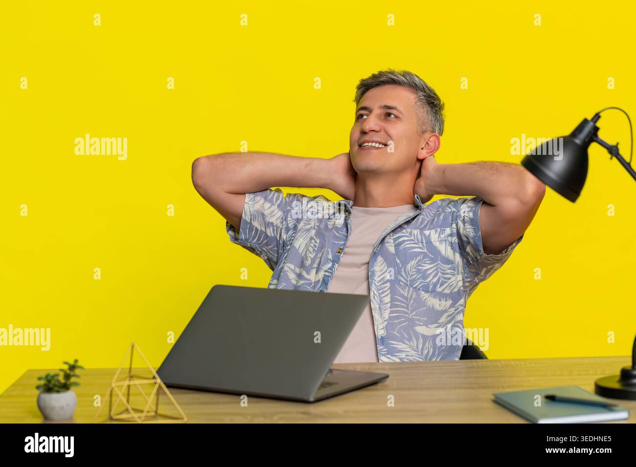 Un uomo di mezza età si è concentrato mentre scriveva sul laptop a tavola, mostrando determinazione e sforzo mentale, quindi si piega tranquillamente indietro in sollievo. Young Guy ha finito il progetto e si è rilassato isolato su sfondo giallo Foto Stock