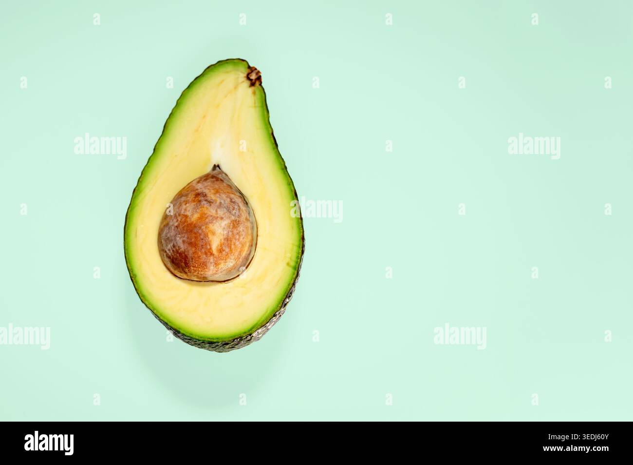Avocado appena tagliato a metà con fossa su sfondo verde menta, girato dall'alto con spazio per copiare sul lato destro. Foto Stock