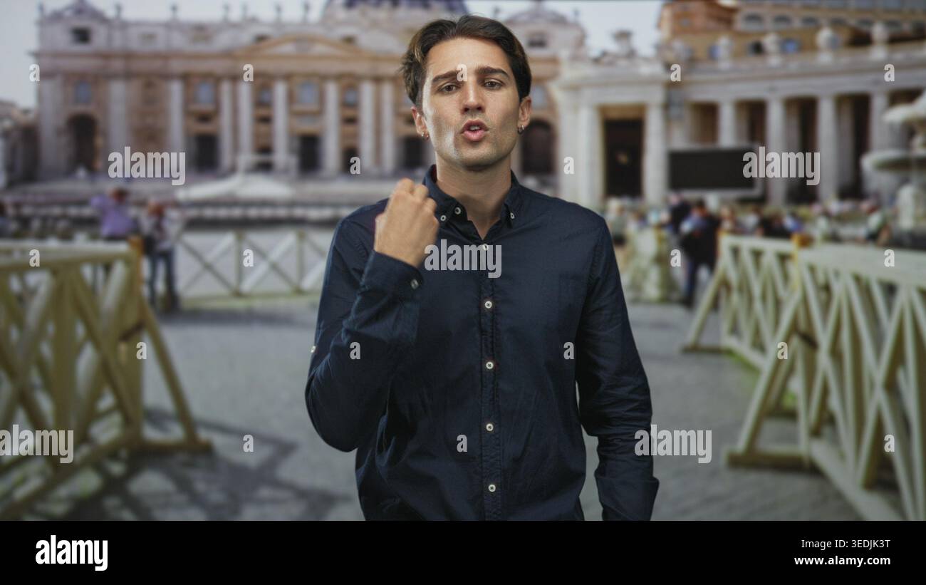 Il giovane punta il dito e mette la mano sul petto mentre parla di fronte a un edificio storico della basilica con folla e barriere; viaggia con informazioni. Foto Stock