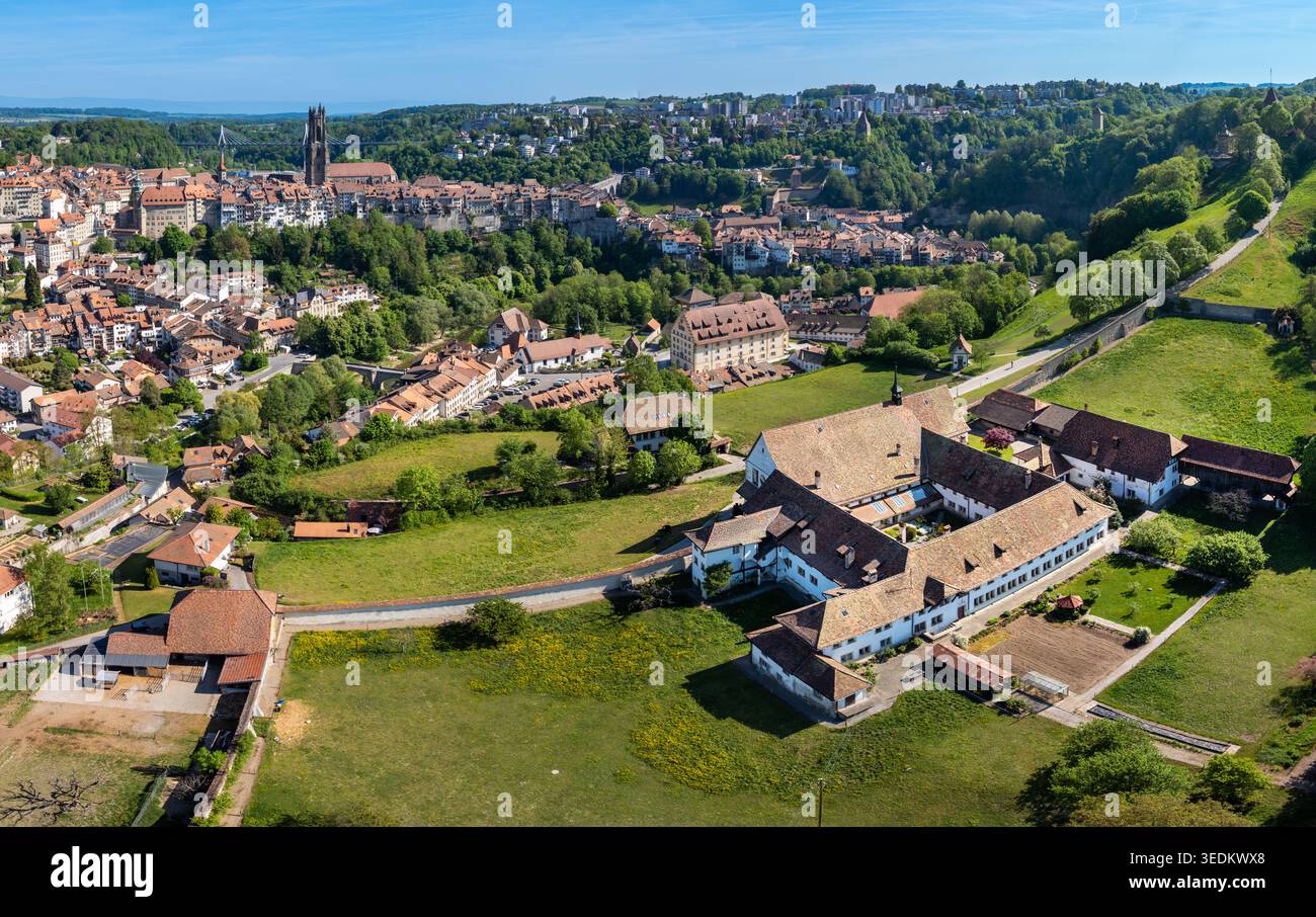 Veduta aerea del Monastere de Montorge circondato da prati verdi con la storica città di Friburgo e la sua cattedrale sullo sfondo sotto una cl Foto Stock