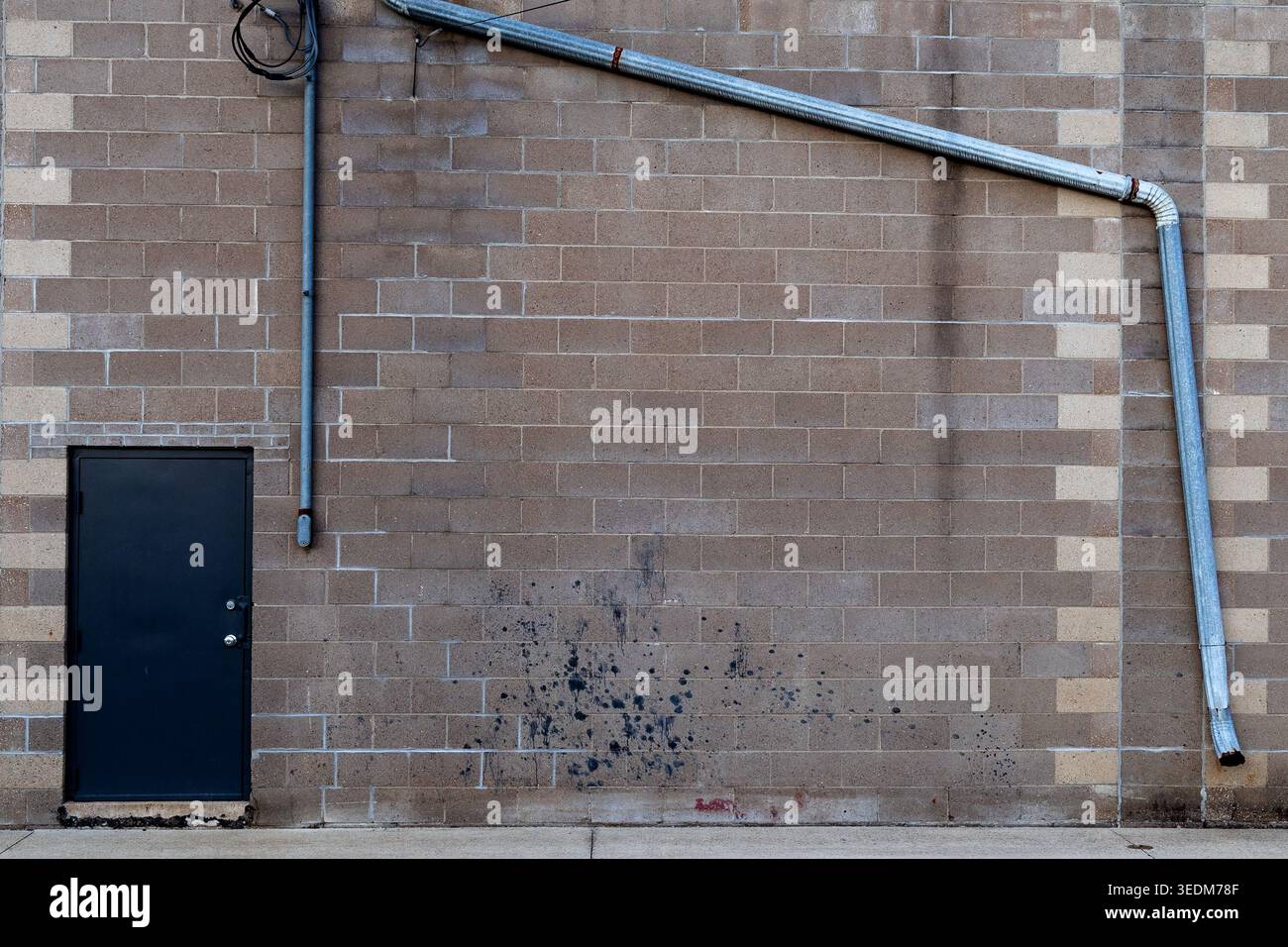 Dubuque, Iowa, Stati Uniti d'America - 25 aprile 2026: Parete industriale in mattoni con porta in metallo nero e tubi a vista nel centro di Dubuque, Iowa Foto Stock