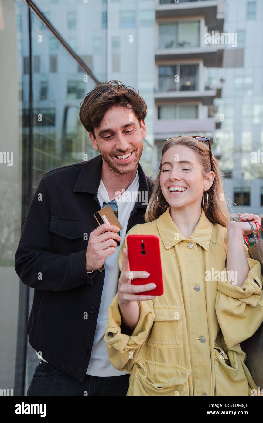 Coppia felice che si gode momenti piacevoli mentre interagisce con lo smartphone e visualizza la carta di credito, mostrando il loro entusiasmo e la loro connessione Foto Stock