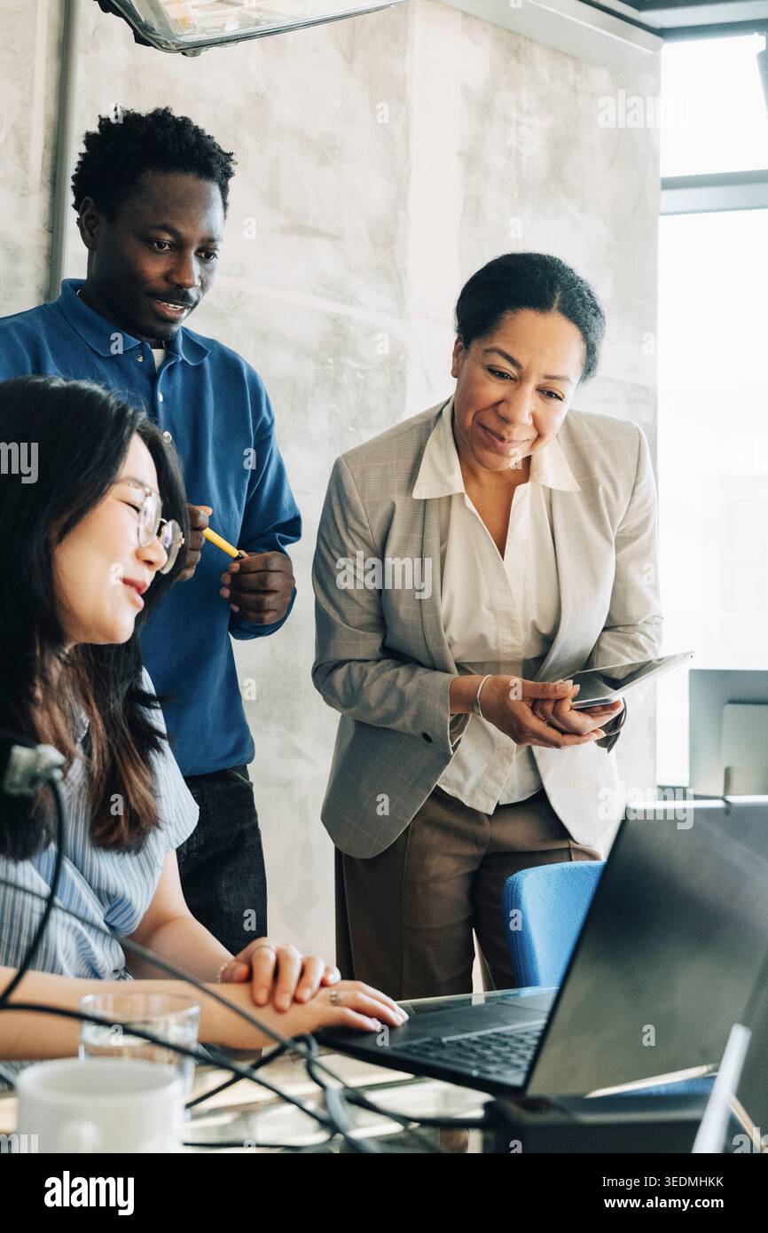 Gruppo di dipendenti sorridenti che esaminano nuove idee mentre si riuniscono intorno al laptop in ufficio Foto Stock