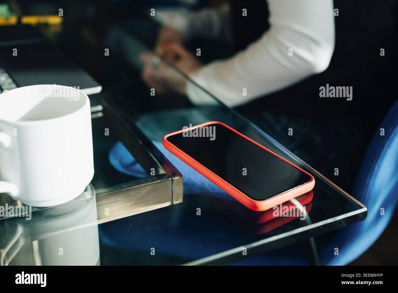 Smartphone con schermo vuoto accanto alla tazza da caffè sulla scrivania in vetro dell'ufficio Foto Stock