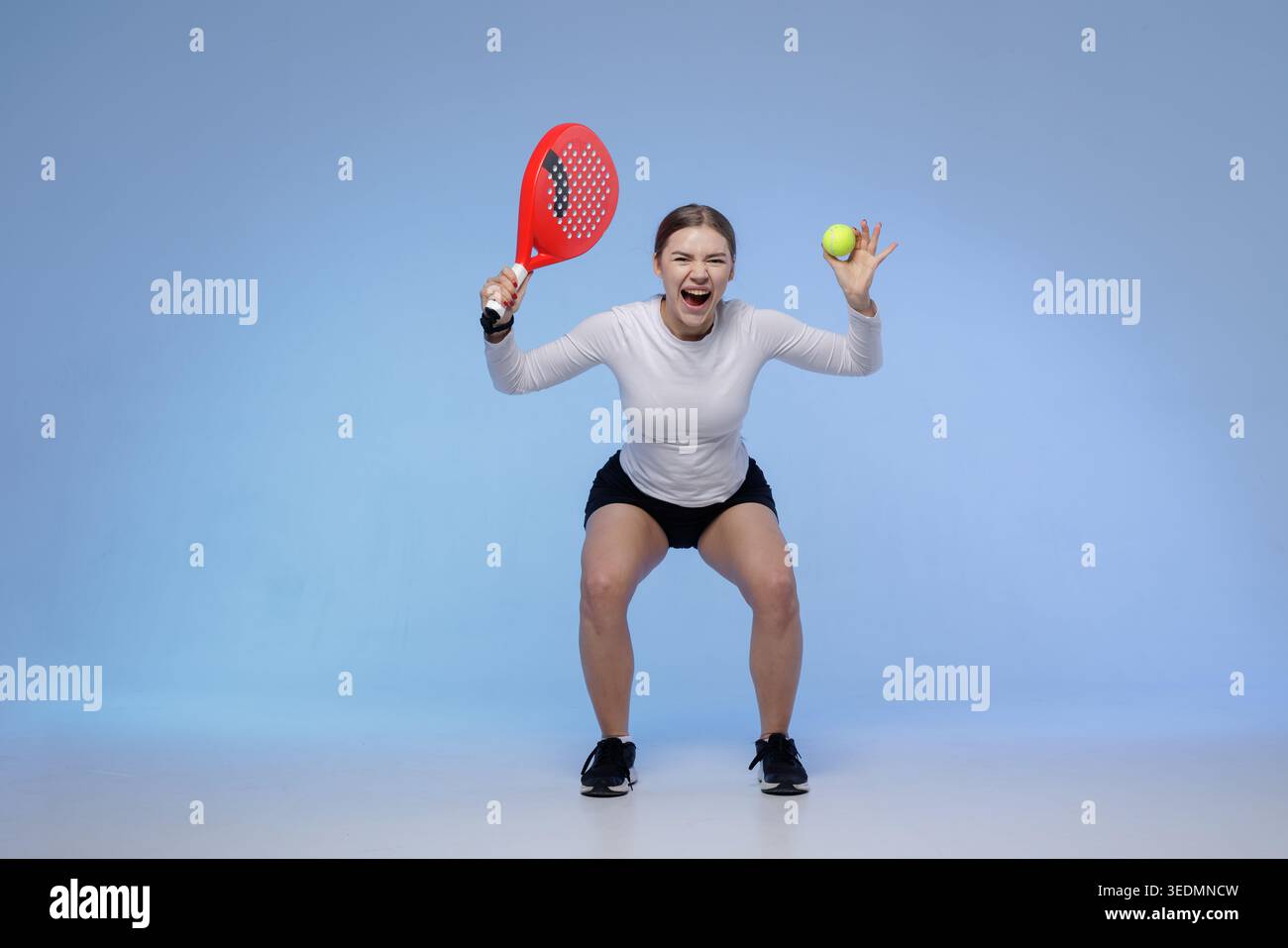 Un'atleta dinamica dimostra entusiasmo mentre pratica il PADEL tennis, tenendo una racchetta e una palla, ideale per la promozione sportiva e il tappetino da allenamento Foto Stock