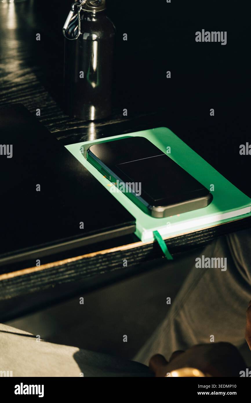 Smartphone appoggiato su un diario floreale verde accanto al computer portatile sulla scrivania dell'ufficio Foto Stock