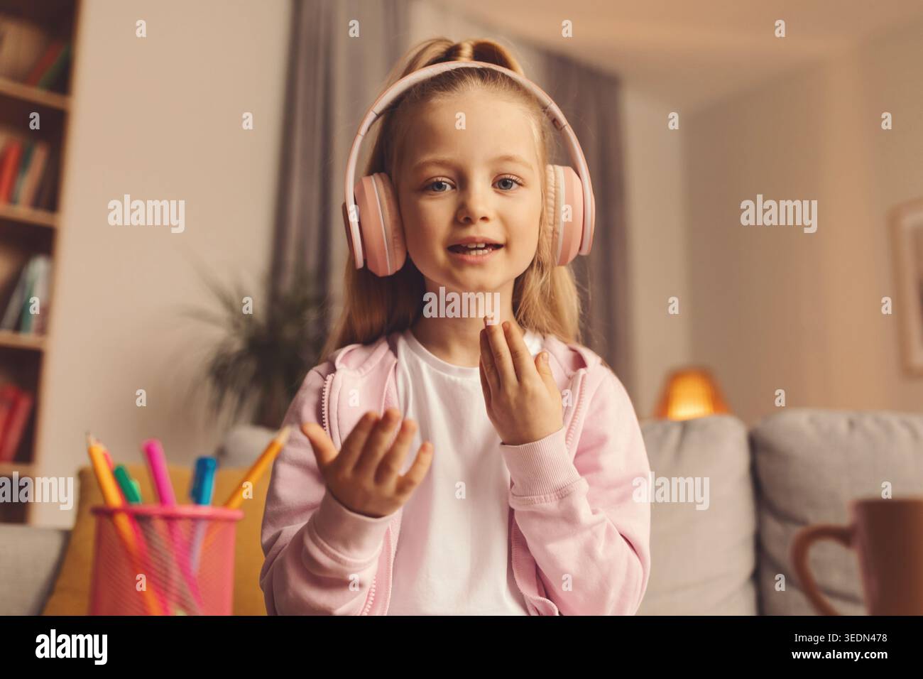 Bambino che indossa le cuffie e siede in salotto sorridendo e gestendo con le mani Foto Stock