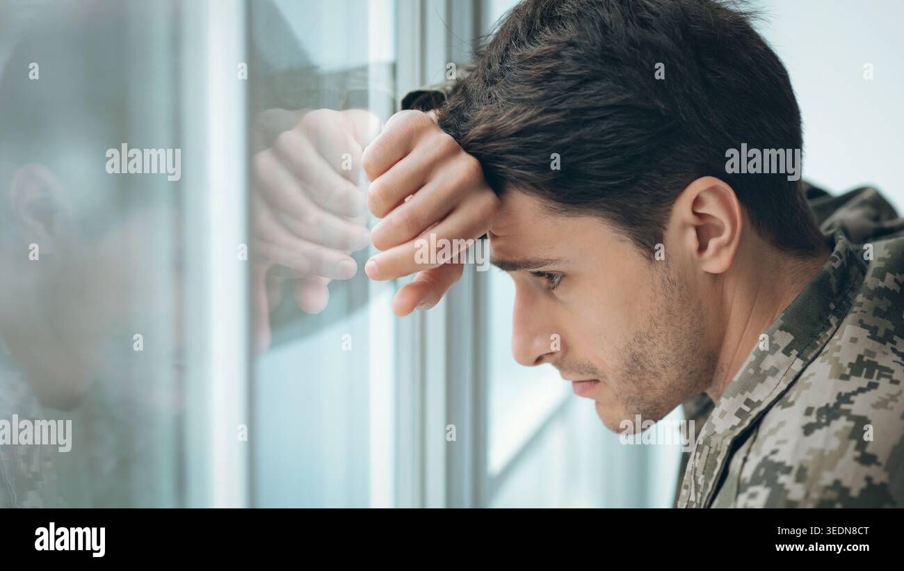 Soldier guarda fuori dalla finestra mentre mostra sentimenti di preoccupazione durante un momento tranquillo Foto Stock