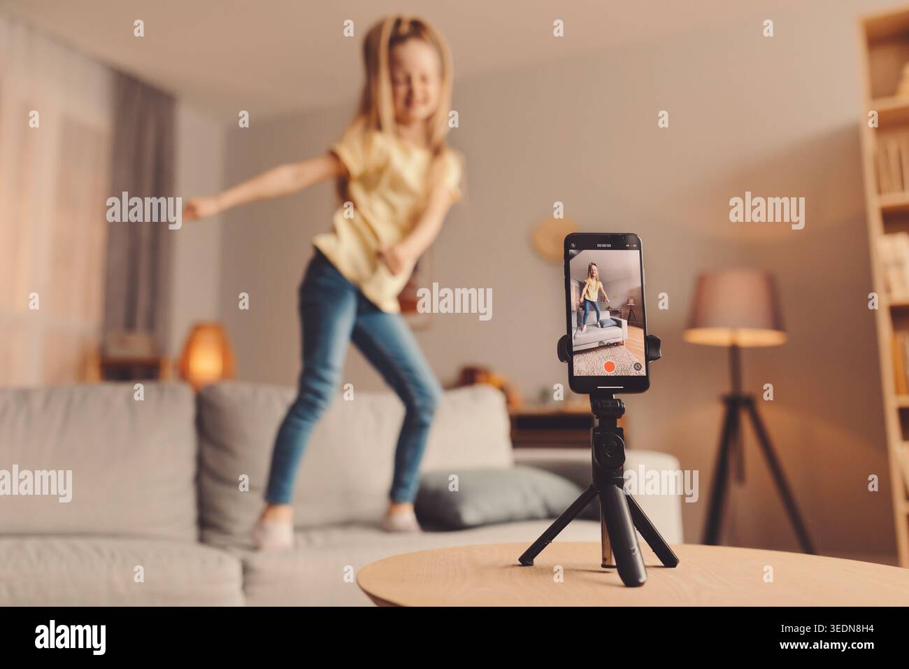 I bambini ballano in salotto mentre registrano video su smartphone montato sul treppiede Foto Stock