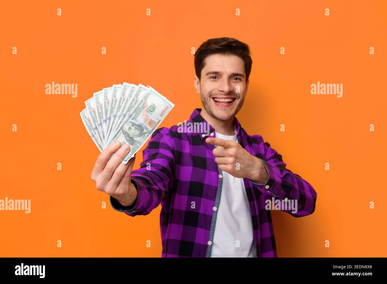 Young Man tiene i soldi mentre sorride su uno sfondo arancione in un ambiente casual Foto Stock