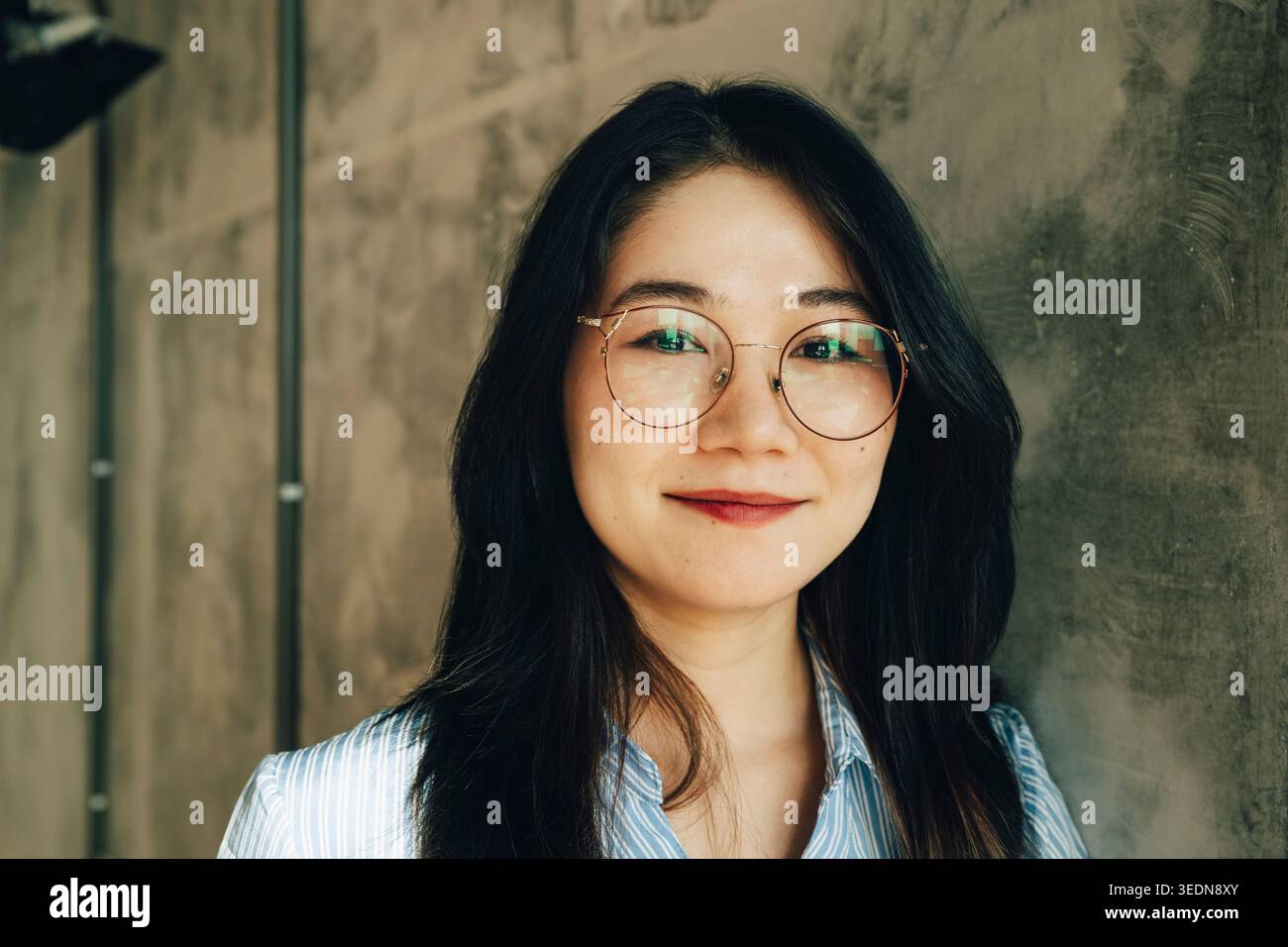 Ritratto di una giovane donna d'affari sorridente appoggiata al muro in ufficio Foto Stock