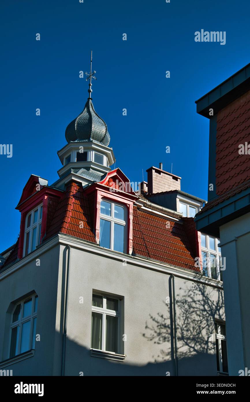 Tetto storico con piastrelle rosse e torretta ornata sul classico edificio urbano europeo contro il cielo blu - la città costiera di Świnoujście. Foto Stock