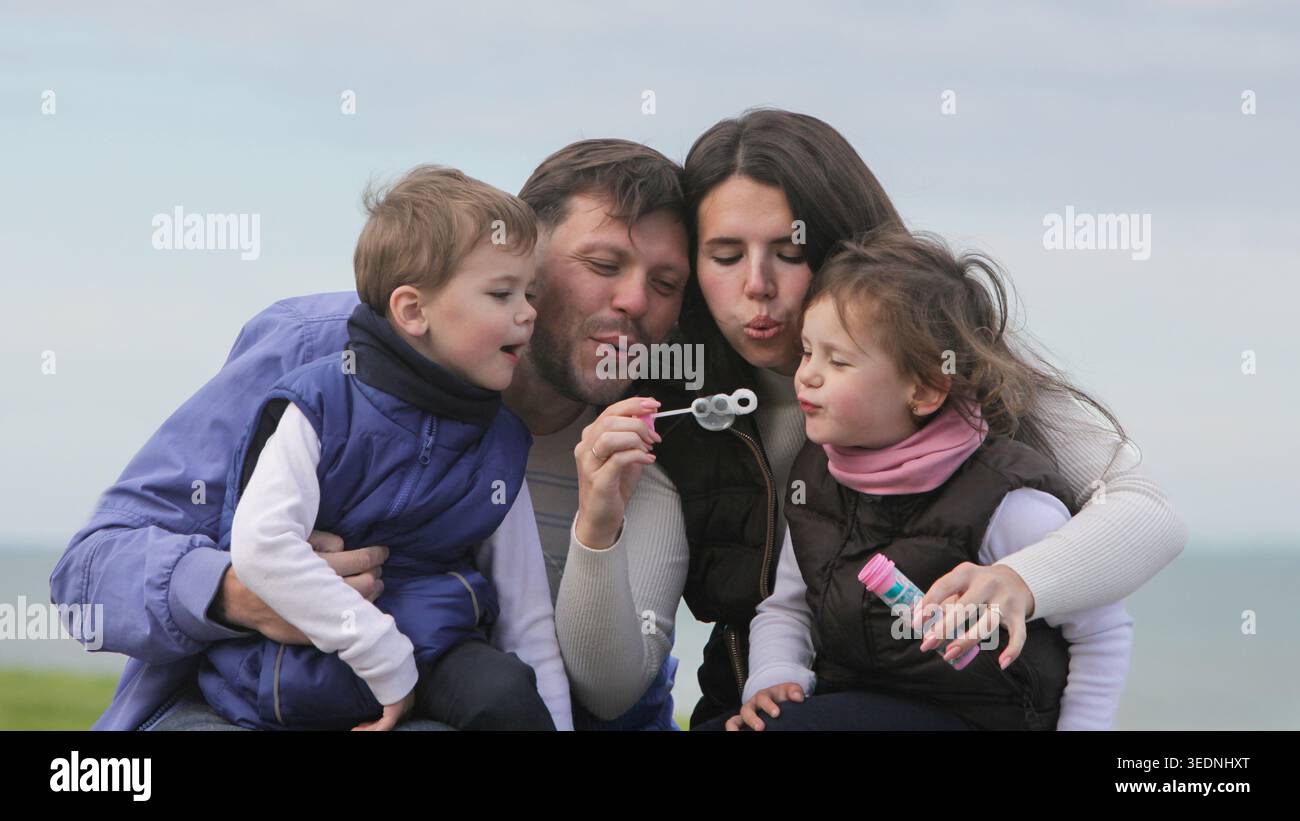 Genitori e bambini si divertono con la famiglia insieme a bolle di sapone all'aperto in un parco in una giornata d'autunno nuvolosa. Foto Stock