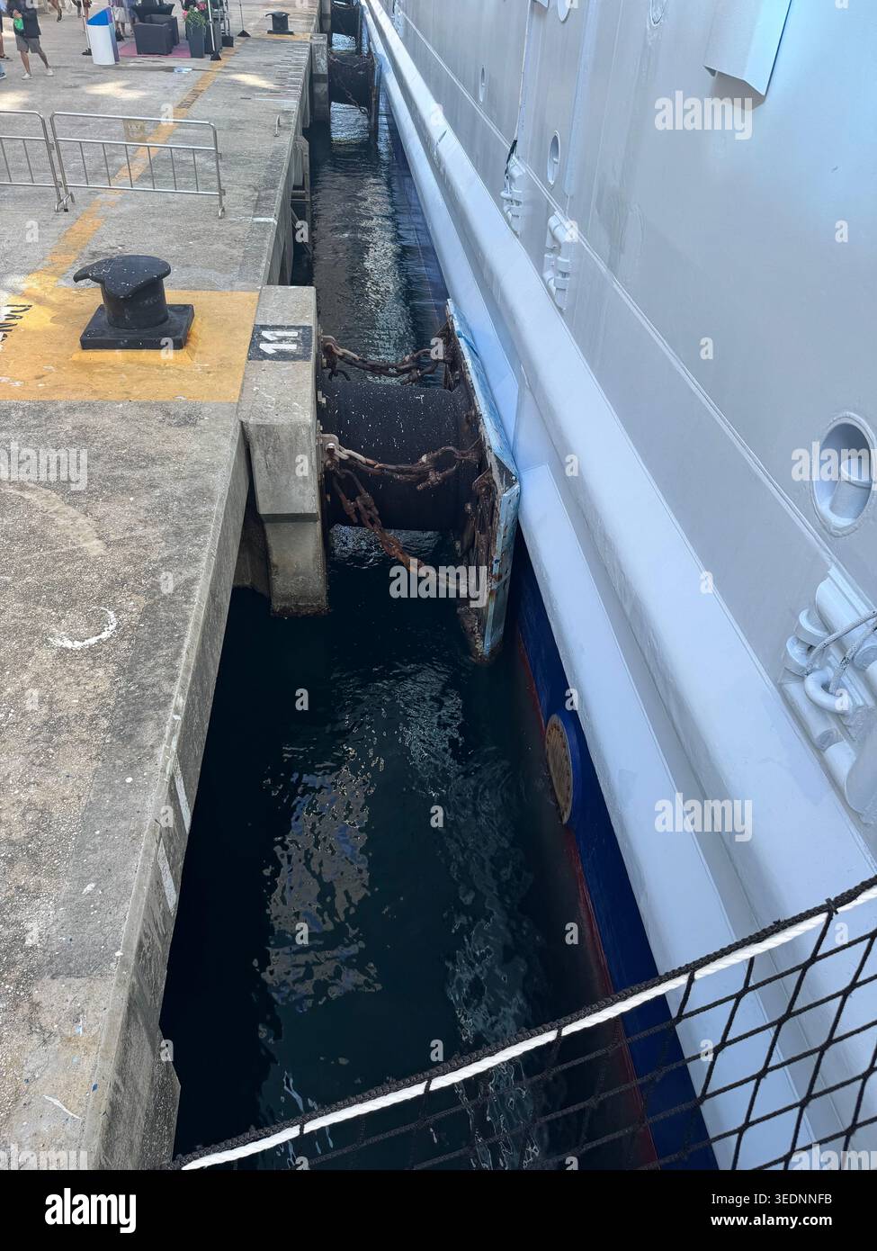 Una visuale stretta e ad alto angolo in basso tra un mega scafo di una nave da crociera attraccata e la parete del molo in cemento. - Immagine stock catturata con smartphone