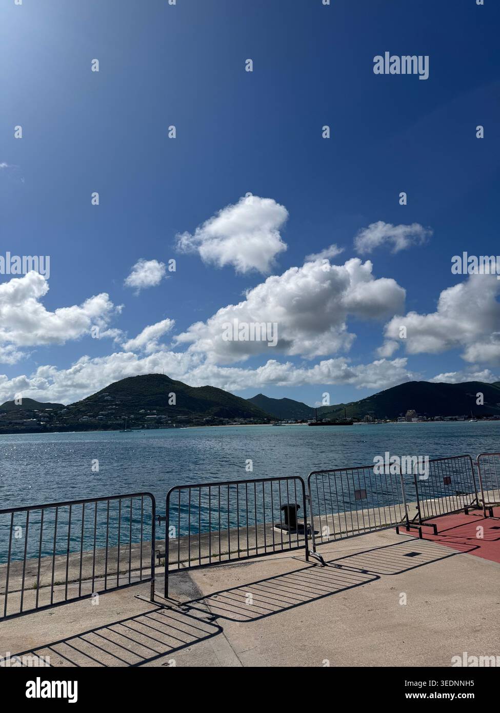 Vista panoramica delle verdi montagne tropicali e della baia blu del mare con nuvole bianche da un molo del porto di Saint Martin. - Immagine stock catturata con smartphone
