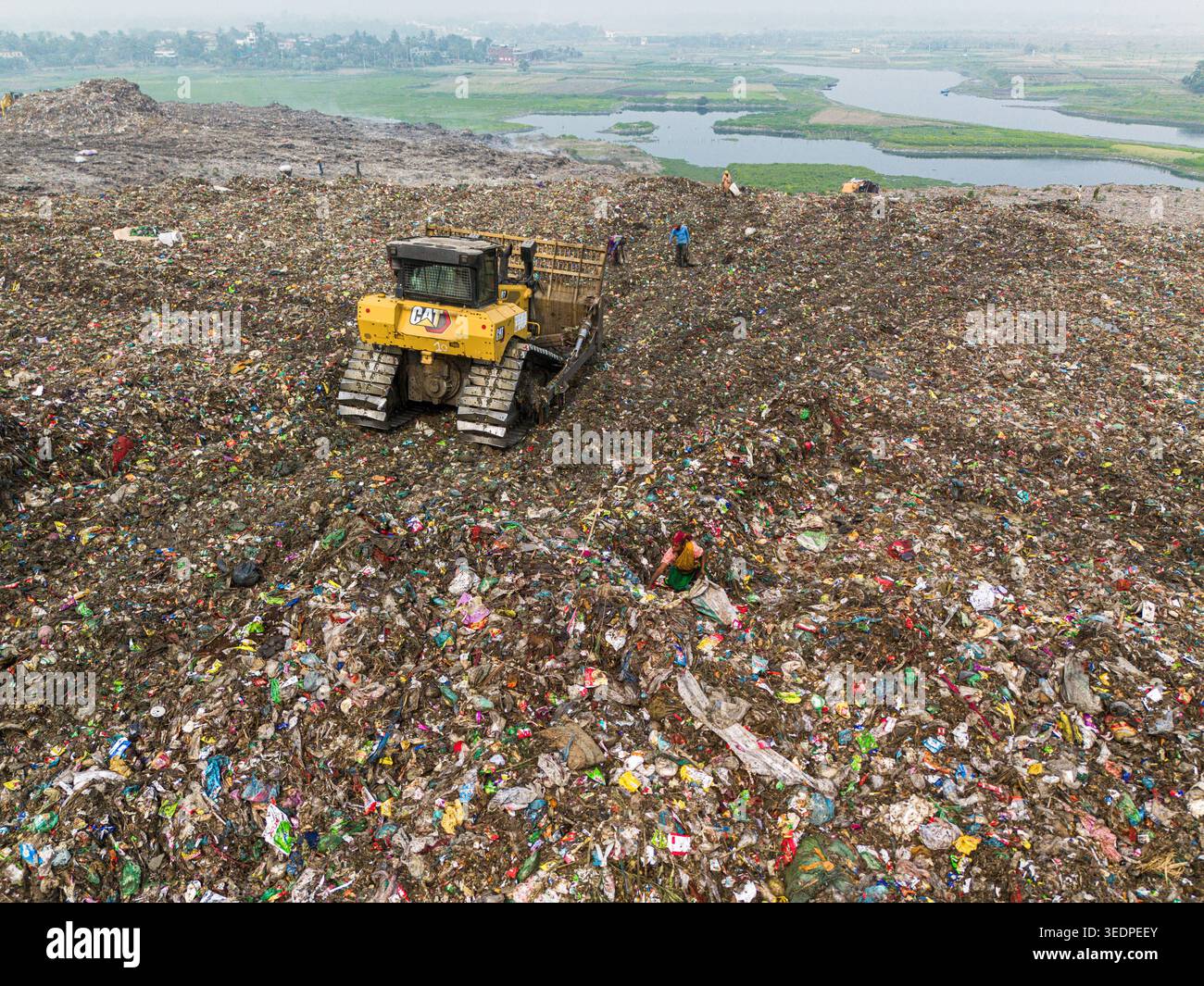 Aminbazar, Bangladesh - 26 gennaio 2025: Veduta aerea di un bulldozer giallo che sposta rifiuti nella discarica di Aminbazar con lavoratori che scavano tra i pali Foto Stock