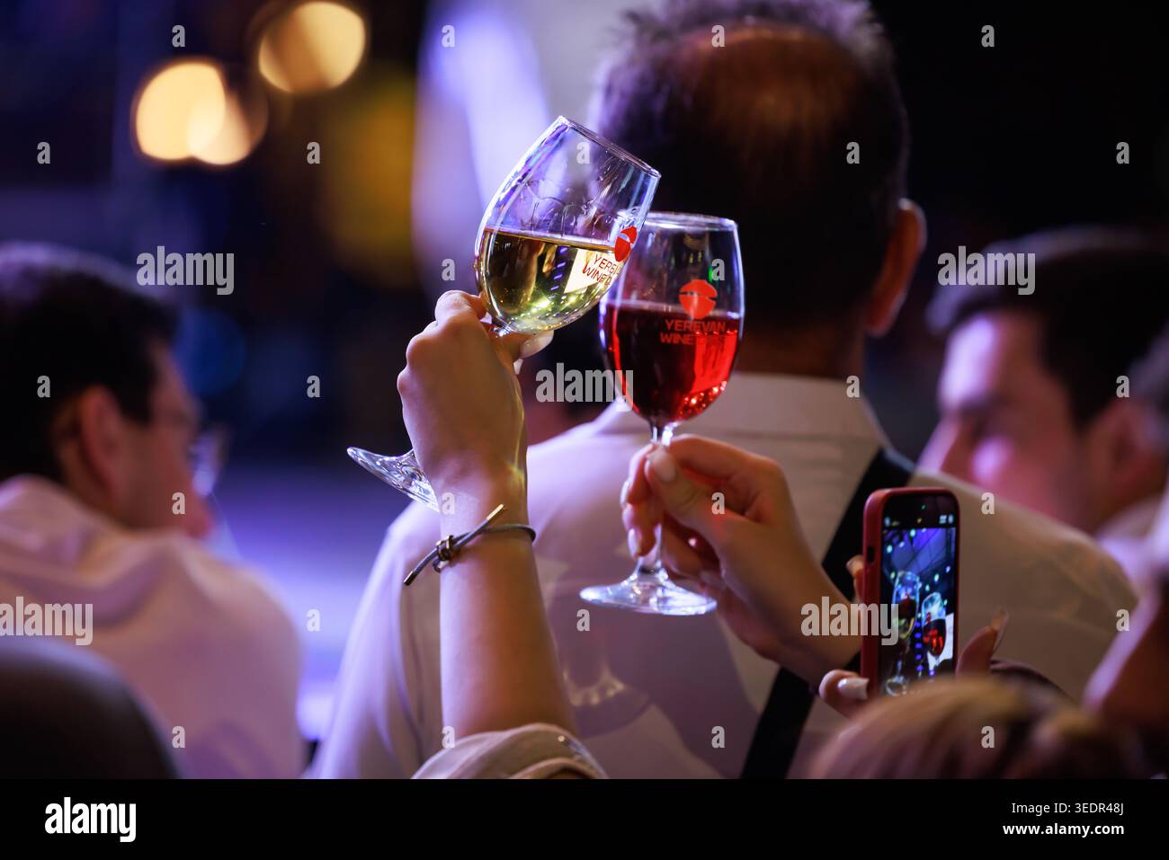 Al Festival del vino di Yerevan riunisce persone che tengono i bicchieri da vino mentre un visitatore cattura il momento con uno smartphone durante il festival. Foto Stock