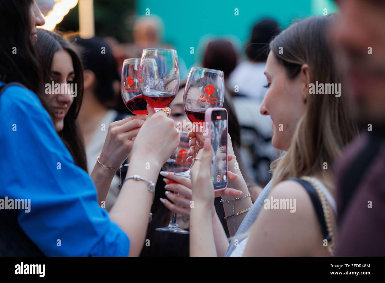A Yerevan Wine Days i visitatori hanno bicchieri di vino rosso mentre un partecipante fotografa il momento con uno smartphone durante il festival a Yerevan. Foto Stock