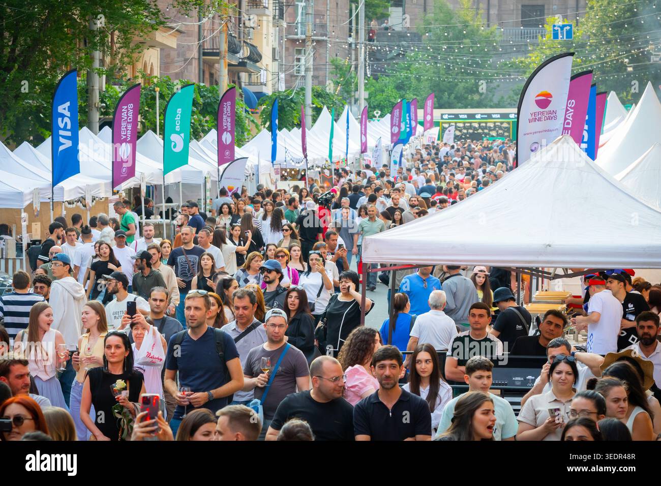Durante l'evento a Yerevan, i visitatori del festival riempiono una strada affollata fiancheggiata da tende da degustazione bianche e bandiere sponsor. Foto Stock