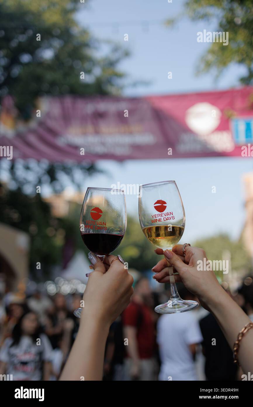 I visitatori del Festival del vino di Yerevan tengono i bicchieri di vino rosso e bianco davanti allo striscione del festival l'8 giugno 2025 a Yerevan, Armenia. Foto Stock