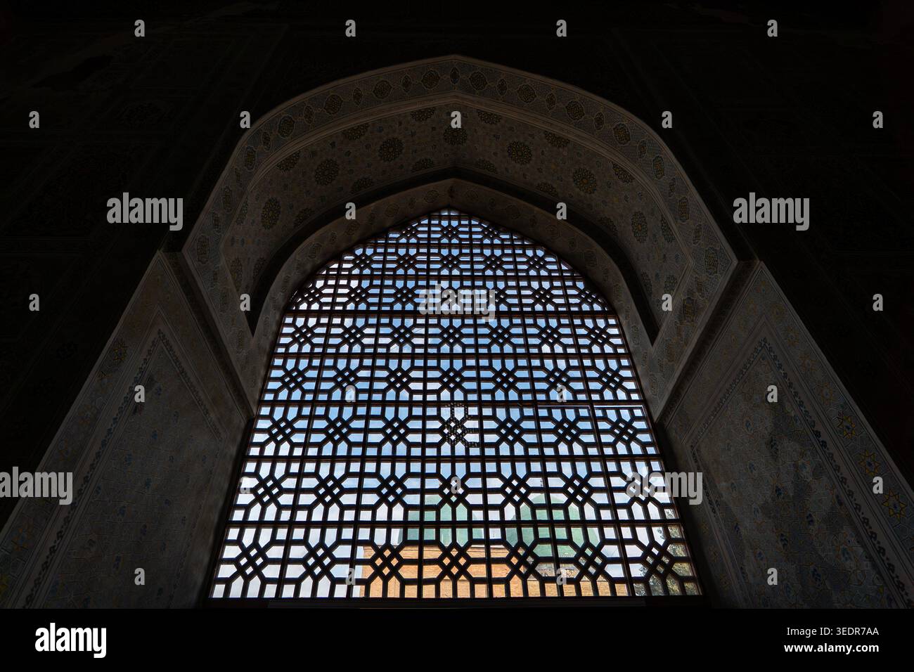 Finestra splendidamente decorata con una griglia ornata e intricati ornamenti a mosaico in una moschea o madrasa a Shakhrisabz, Uzbekistan. Foto Stock