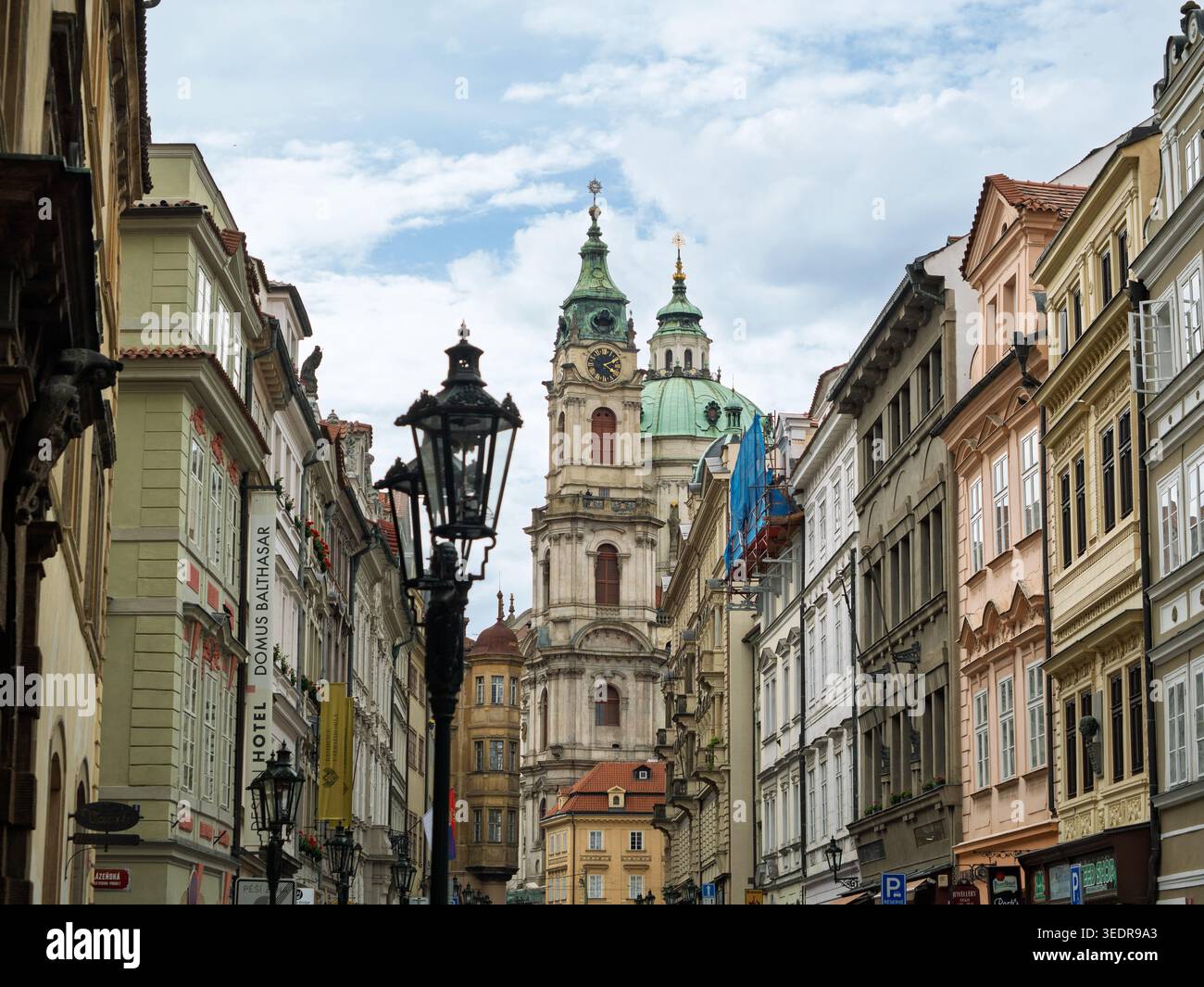 Ammira Una stretta strada storica con le tradizionali case a schiera barocche e il dominante Duomo della Chiesa di San Nicola, Praga, Repubblica Ceca. Foto Stock