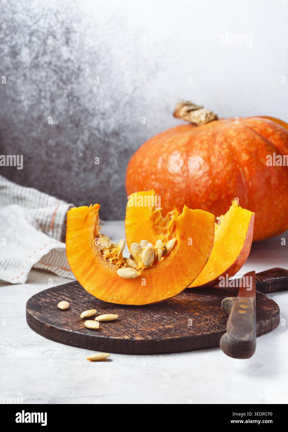 Fette di zucca Mooregold (Cucurbita maxima) su una tavola di legno con un coltello e una zucca intera. Cucina rustica con un vivace autunno arancione Foto Stock