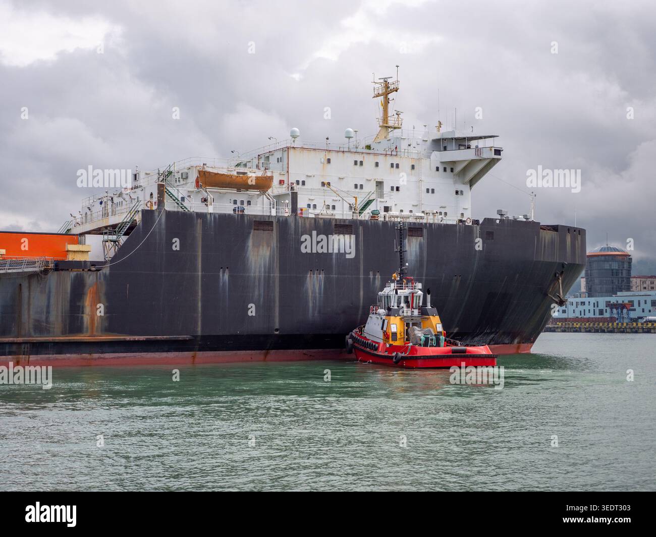 Rimorchiatore logistico marittimo che guida una massiccia nave da carico in un porto marittimo tempestoso, spedizioni globali, operazioni portuali, trasporto industriale, catena di approvvigionamento. Foto Stock