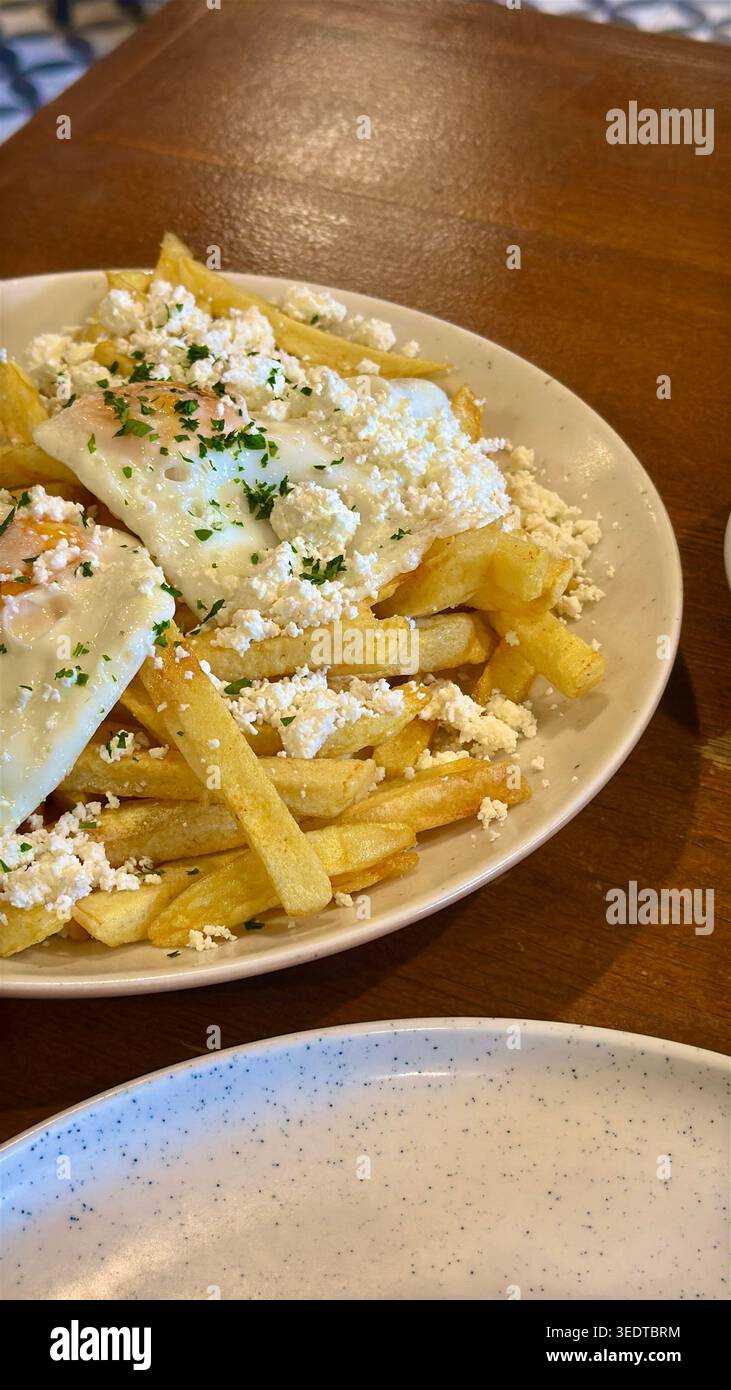 Piatto di patatine fritte croccanti sormontate da un uovo fritto, formaggio grattugiato ed erbe fresche, servito come un pasto sostanzioso di comfort food, piatto della cucina rumena. Foto Stock