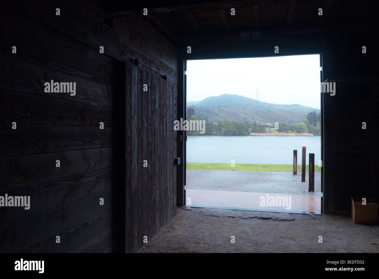 Cromwell, nuova Zelanda: Guardando attraverso l'interno scuro di un rustico capannone di legno verso le acque luminose e le colline del lago Dunstan Foto Stock
