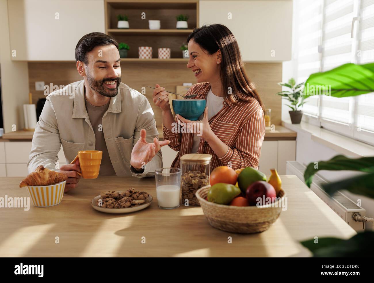 Un uomo e una donna fanno colazione in cucina. Si sorridono mentre condividono cibo e bevande a tavola. Foto Stock