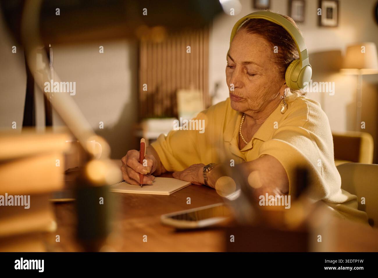 Donna anziana che indossa le cuffie scrivendo note per l'apprendimento online Foto Stock