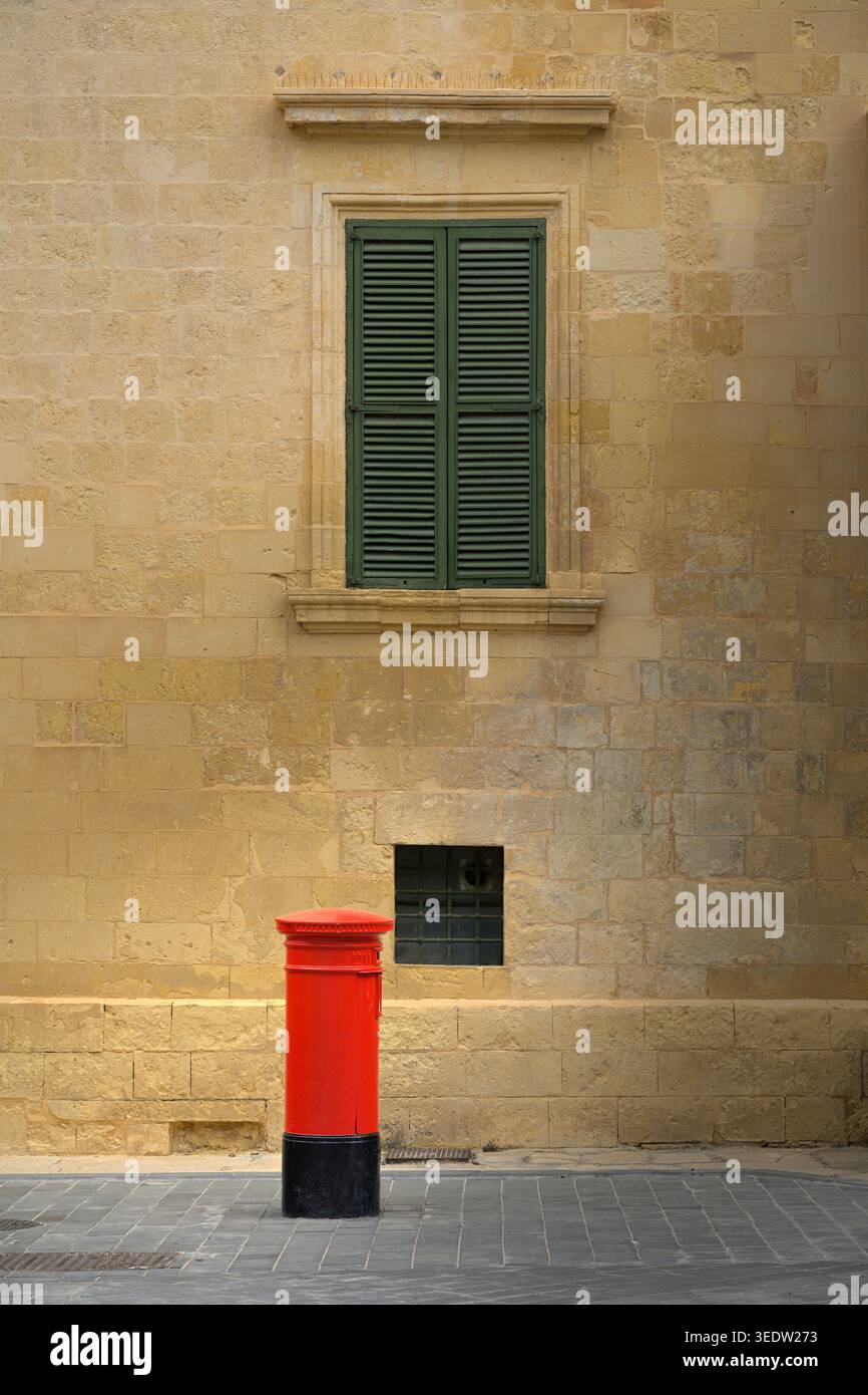 Una tradizionale scatola rossa per posta con architettura in pietra calcarea sullo sfondo a la Valletta, Malta. Foto Stock