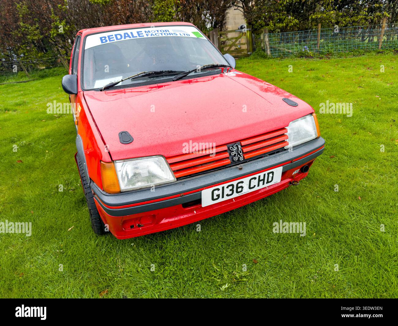 Red Peugeot 205 auto da rally con modifiche agli sport motoristici e sponsorizzazione Sun strip parcheggiata su un campo erboso nel Regno Unito - Immagine stock catturata con smartphone