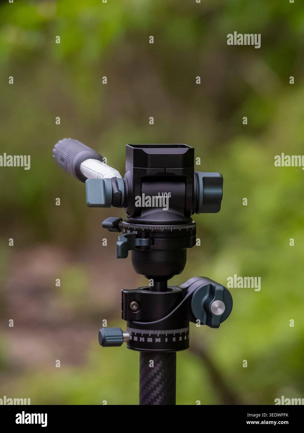 Primo piano della testa di un treppiede gimbal professionale nero con manopole di regolazione e scala panoramica su una gamba in fibra di carbonio sullo sfondo di una foresta sfocata Foto Stock