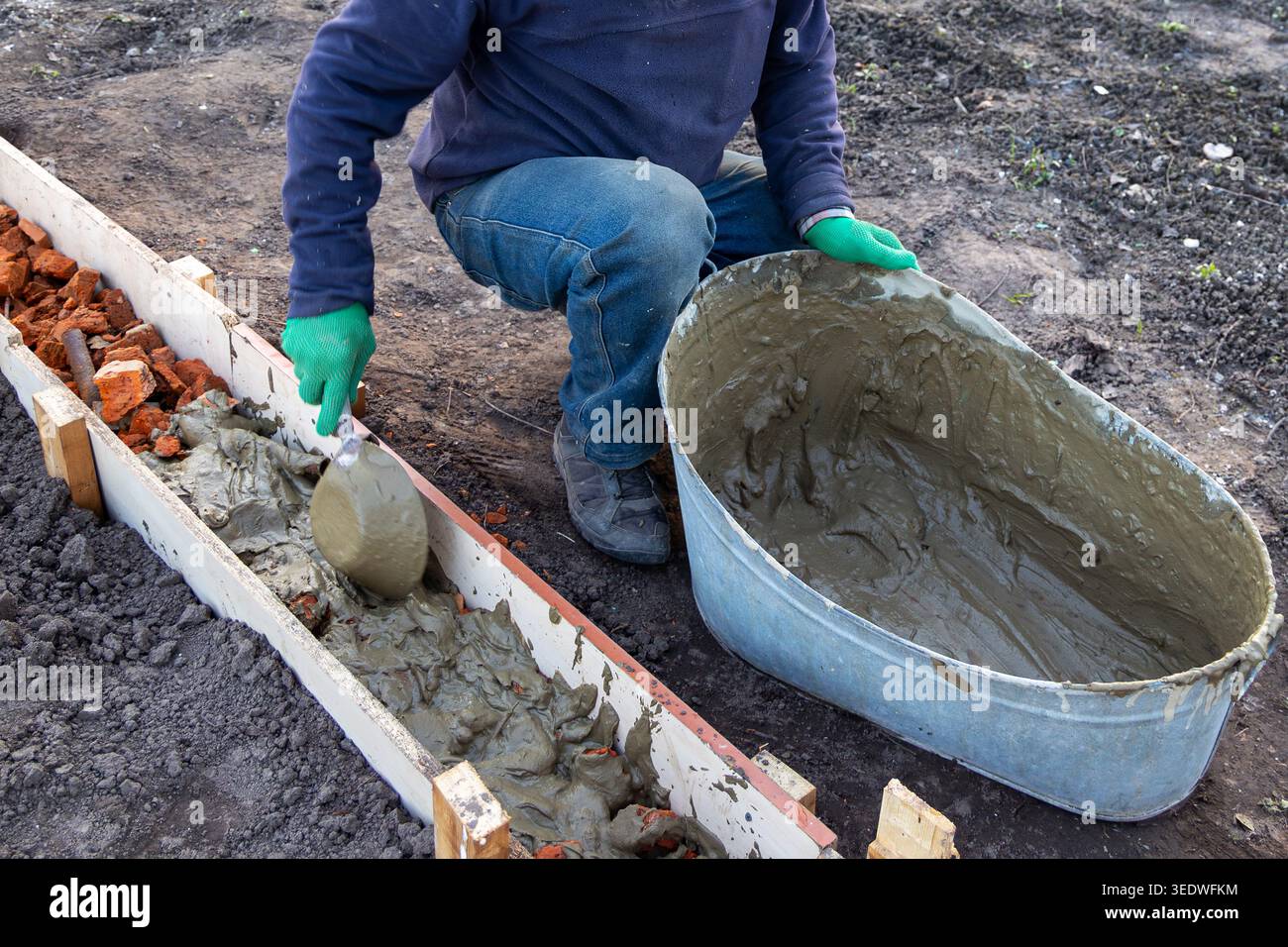 Lavoratore che versa Malta nella forma della Fondazione. Il lavoratore riempie la cassaforma di legno con Malta bagnata e macerie di mattoni durante la preparazione di un piccolo calcestruzzo esterno Foto Stock