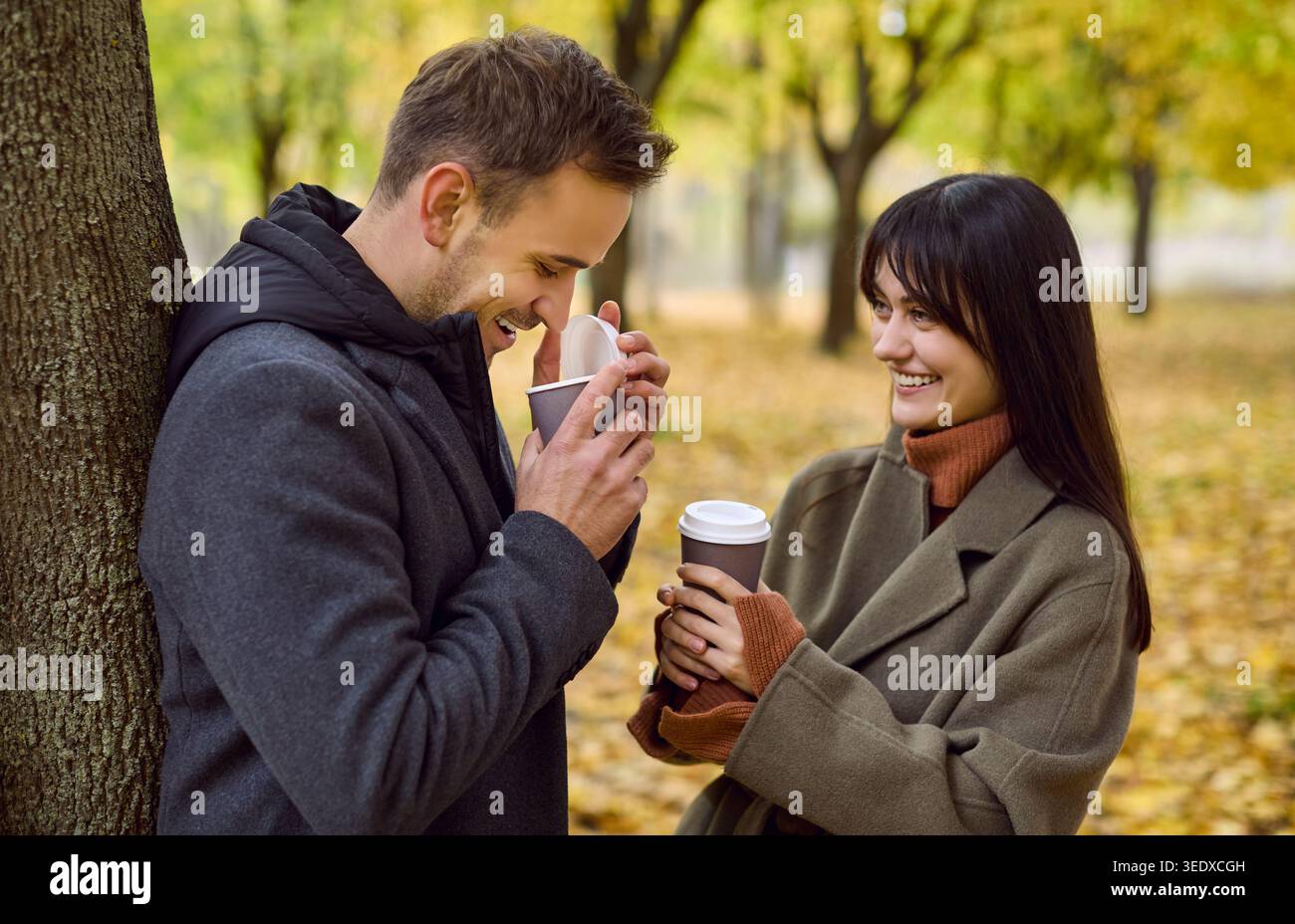 Coppia felice che beve caffè nel parco autunnale, condividendo calore e benessere mentale Foto Stock
