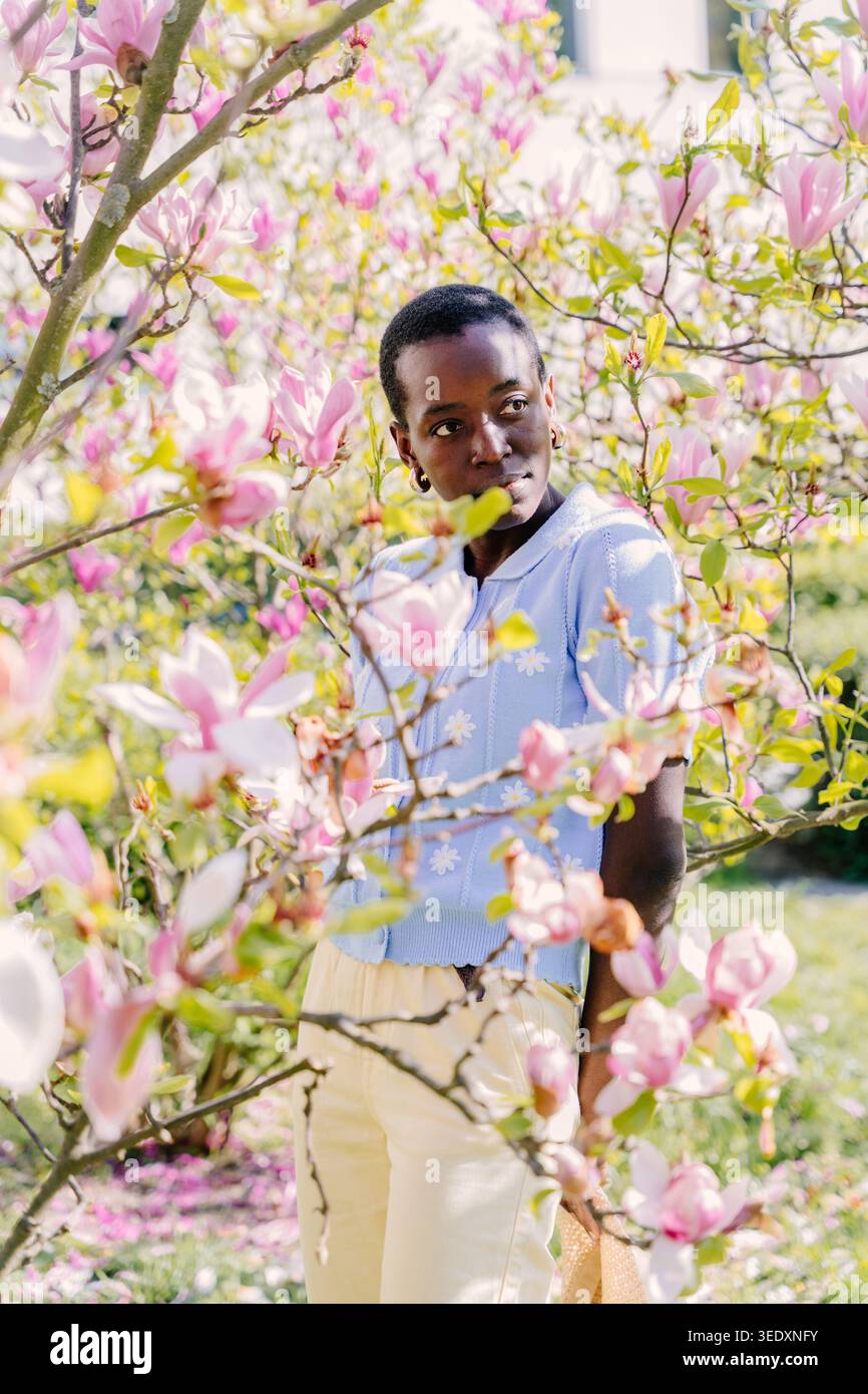 Giovane donna africana che guarda attraverso i rami di Magnolia nel Sunny Spring Park Foto Stock