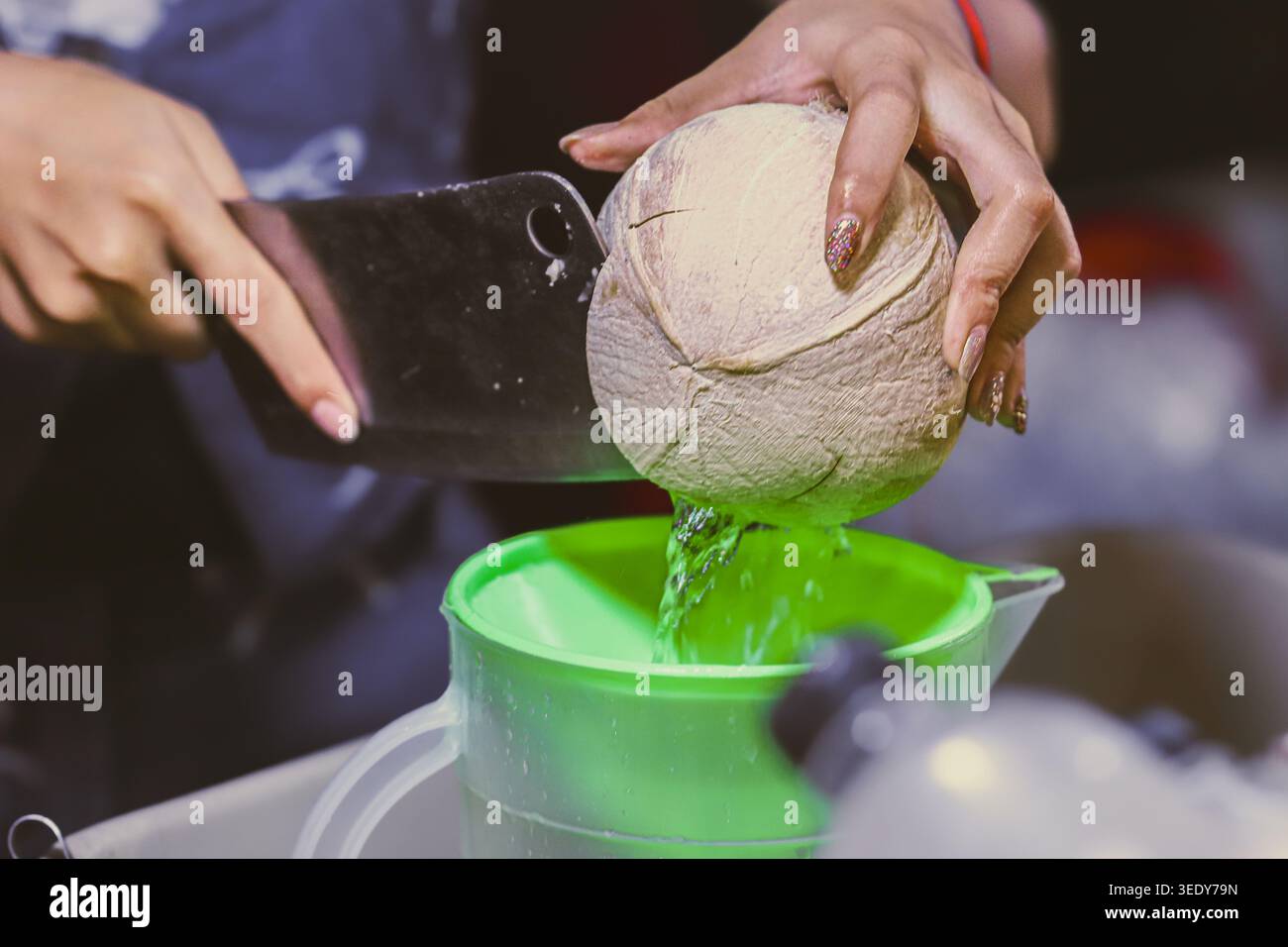 Acqua fresca di cocco versata in un imbuto in un mercato thailandese locale. Autentico cibo di strada e idratazione tropicale naturale per i viaggi estivi. Foto Stock