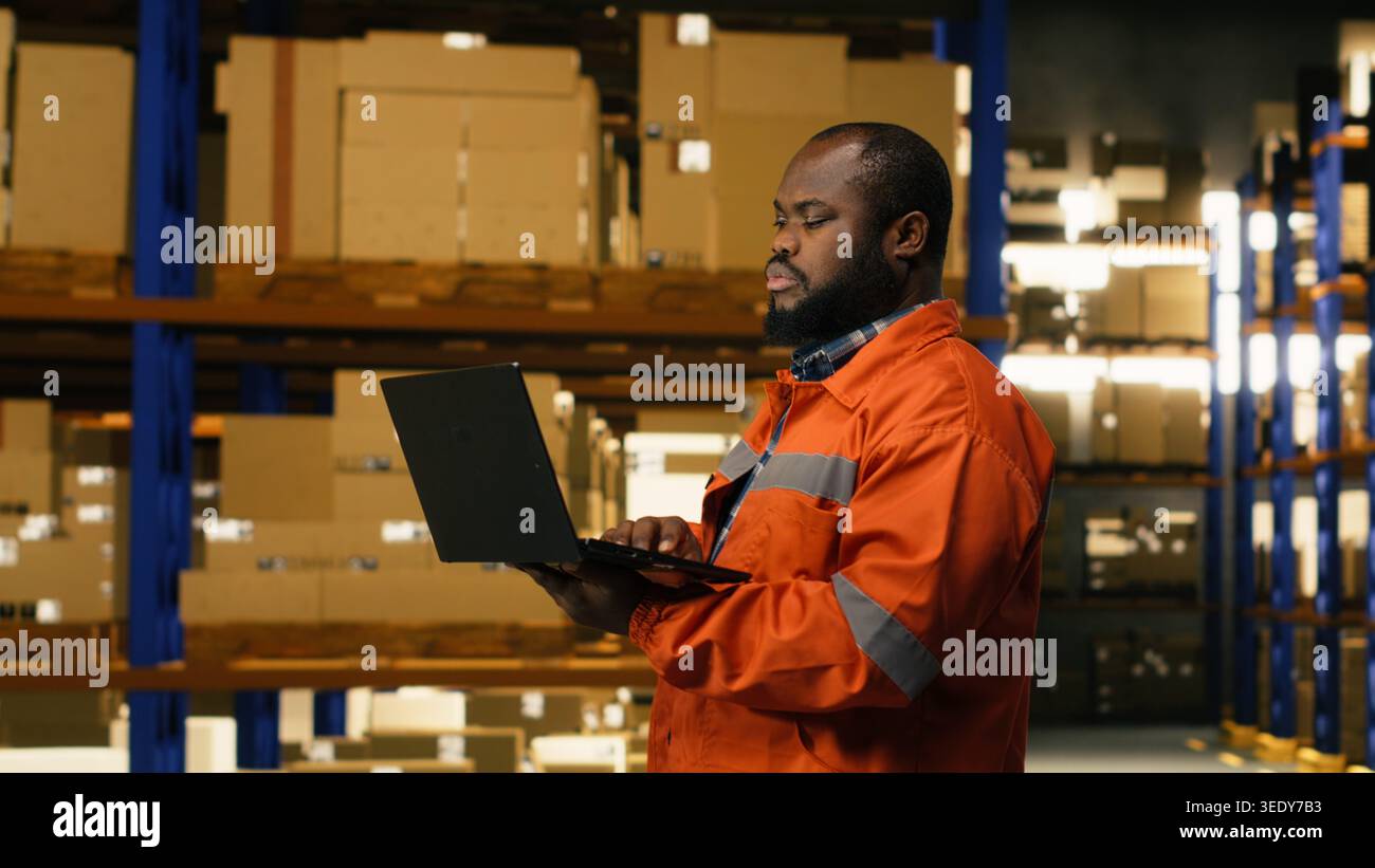Evasione degli ordini su computer portatile, personale afroamericano, gestione delle spedizioni da parte dei dipendenti in impianti industriali, con pacchi e merci. Consegna rapida e operazioni di deposito e-commerce. Foto Stock