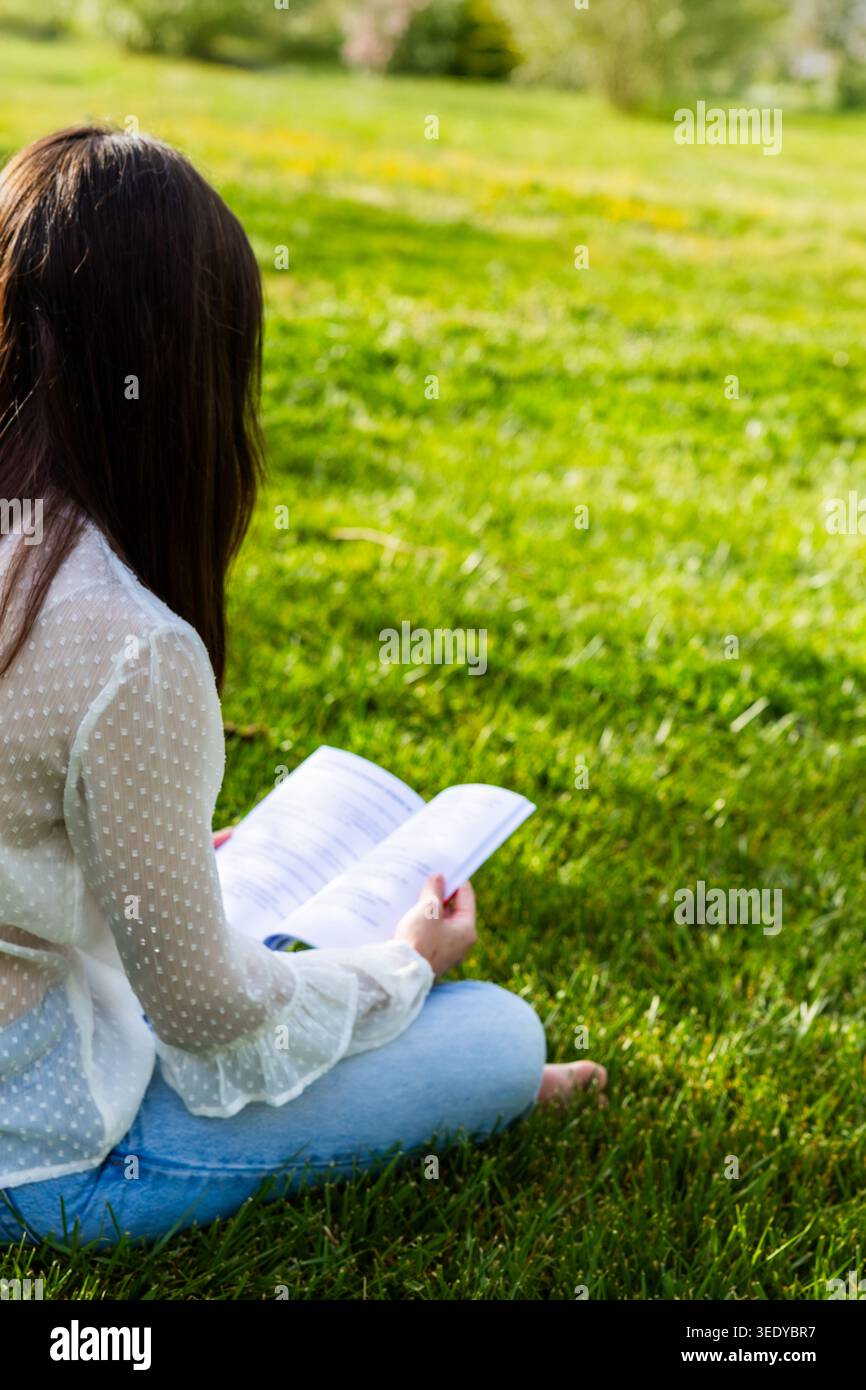 Donna che studia all'aperto leggendo carta in erba verde Foto Stock