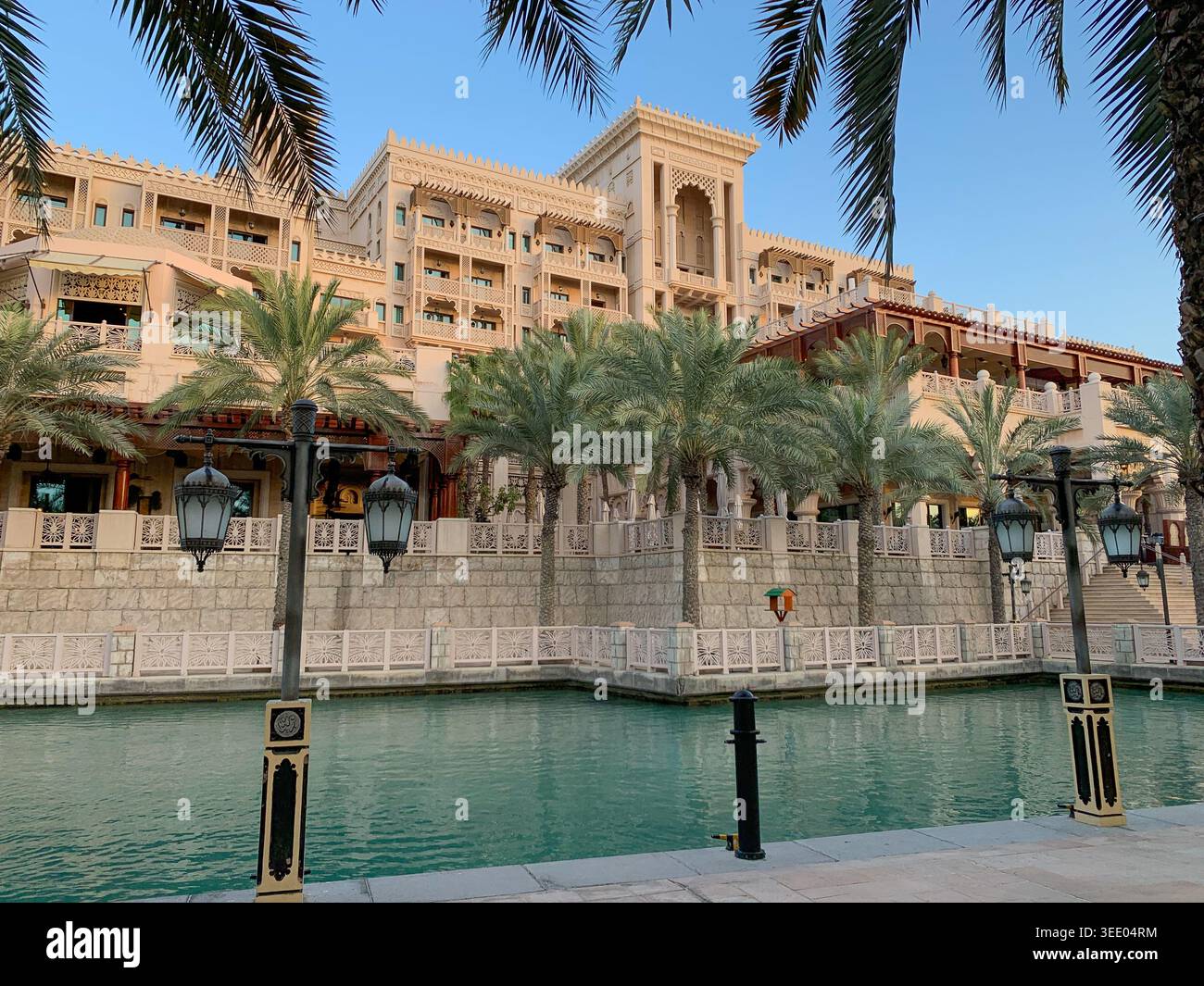 Vista della tradizionale architettura araba con palme e lanterne lungo un canale d'acqua turchese a Dubai, Dubai, Emirati Arabi Uniti. Foto Stock