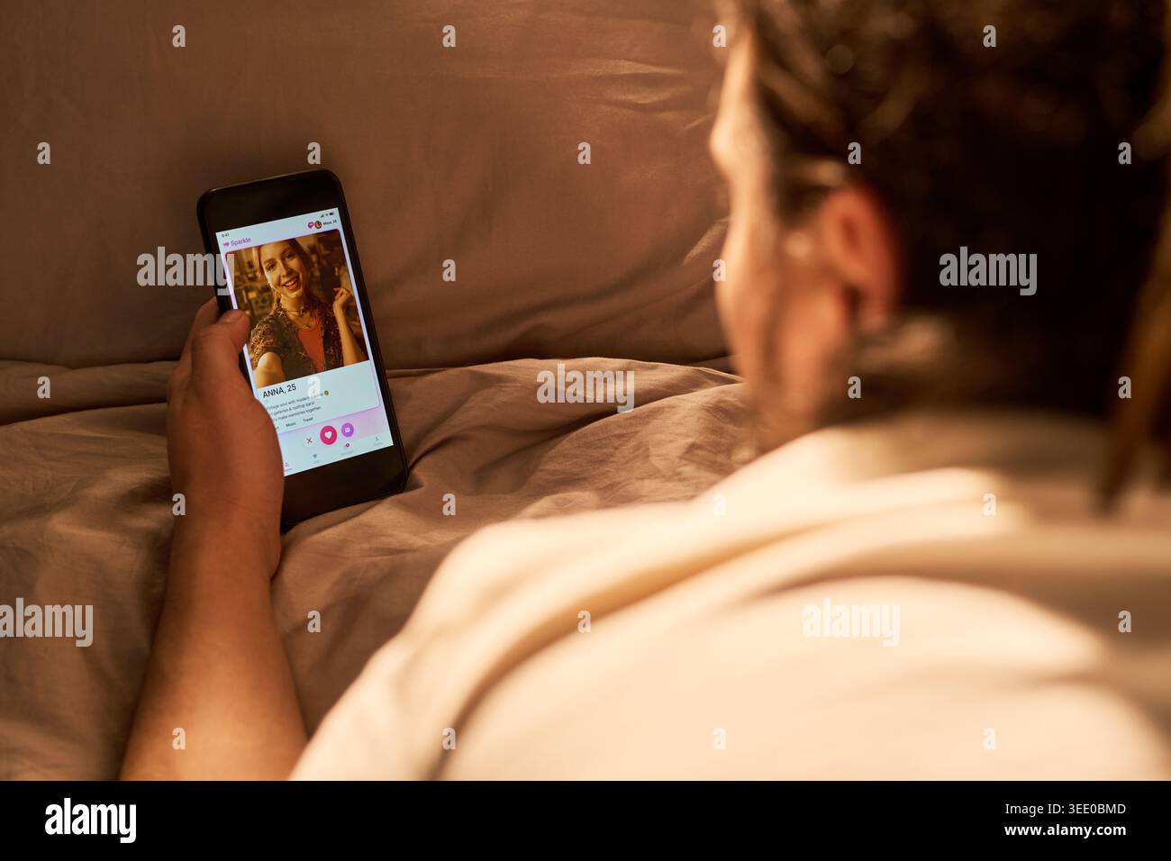 Vista a spalla di un giovane uomo adulto che naviga nell'app di incontri sullo smartphone a letto, profilo di scorrimento corrispondente. Ideazione di romanticismo online, utile per incontri digitali o marketing di relazioni Foto Stock
