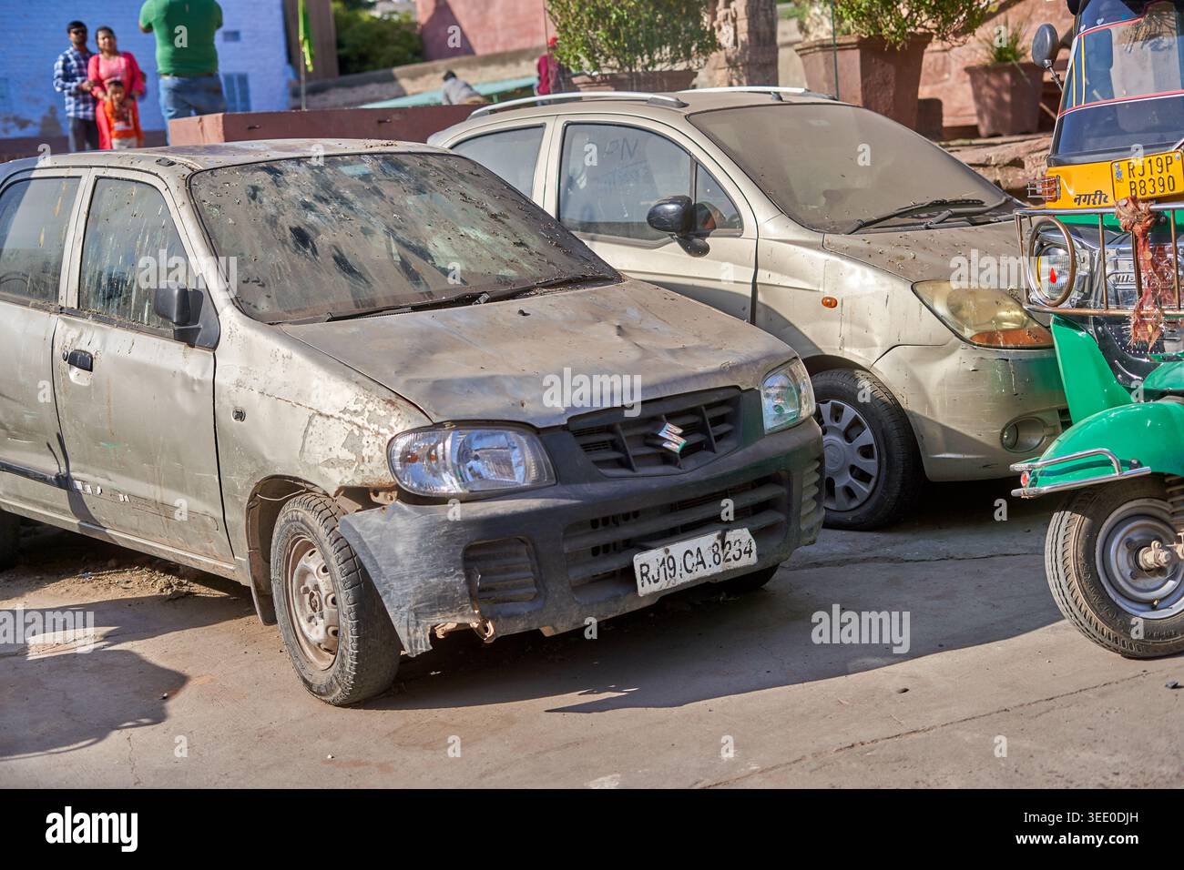 Una scena di strada nel Rajasthan, India, con due auto a portiere posteriori polverose e consumate parcheggiate sul ciglio della strada. In primo piano c'è una Suzuki Alto argentata con Foto Stock