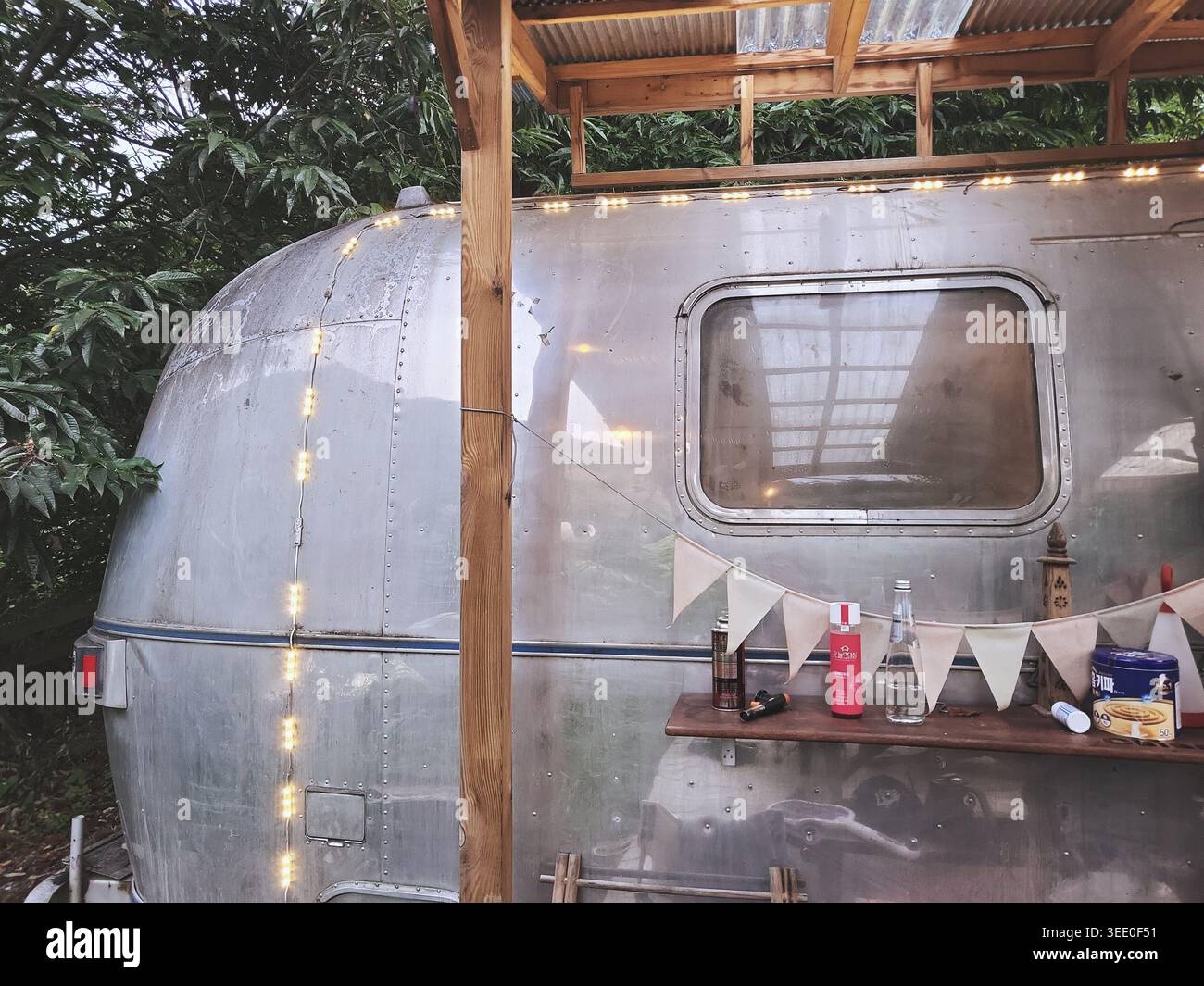 Rimorchio camper d'epoca circondato dalla vegetazione della foresta durante una tranquilla esperienza di glamping. Foto Stock